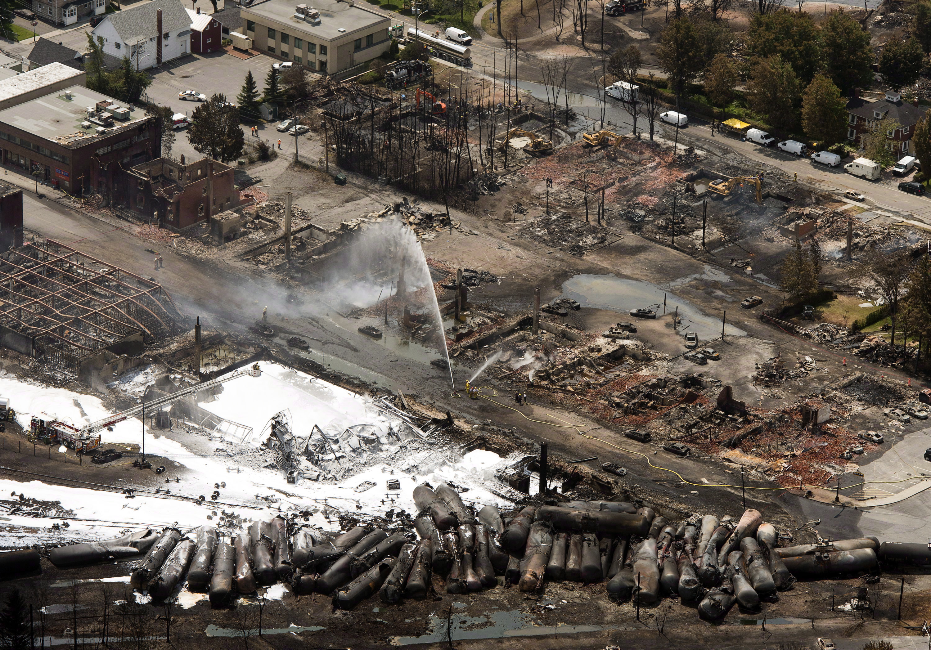 In this Sunday, July 7, 2013 photo, the downtown core is in ruins as firefighters water smoldering rubble in Lac-Megantic, Quebec, after a train derailed, igniting tanker cars carrying crude oil. Lac-Megantic still struggles to recover as it marks the disaster's one-year anniversary. (AP Photo/The Canadian Press, Ryan Remiorz) (AP)