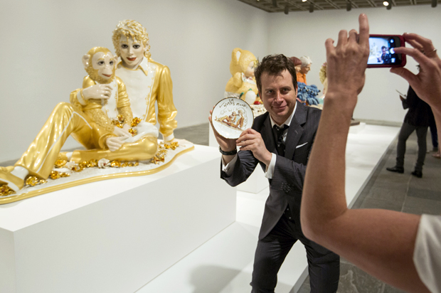 A man holds a signed plate with the likeness of the sculpture Michael Jackson and Bubbles in front of the actual sculpture at the Jeff Koons retrospective at the Whitney Museum of American Art in New York June 24, 2014. (Reuters/Lucas Jackson)