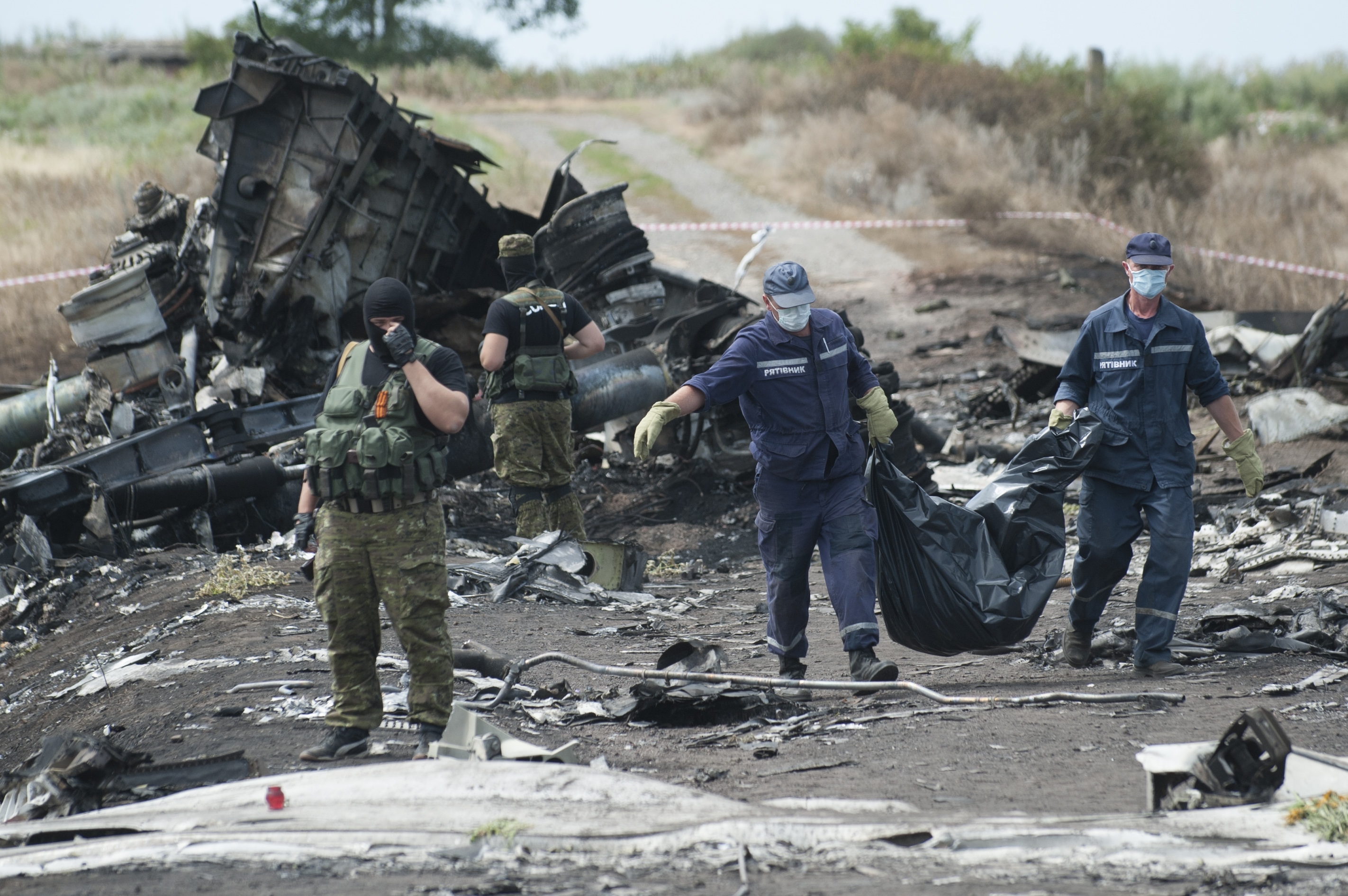 Ukrainian Emergency workers carry a stretcher with a victim's body in a bag as pro-Russian fighters stand in guard at the crash site of Malaysia Airlines Flight 17 near the village of Hrabove, eastern Ukraine, Sunday, July 20, 2014. Rebels in eastern Ukraine took control Sunday of the bodies recovered from downed Malaysia Airlines Flight 17, and the U.S. and European leaders demanded that Russian President Vladimir Putin make sure rebels give international investigators full access to the crash site. ((AP Photo/Evgeniy Maloletka))