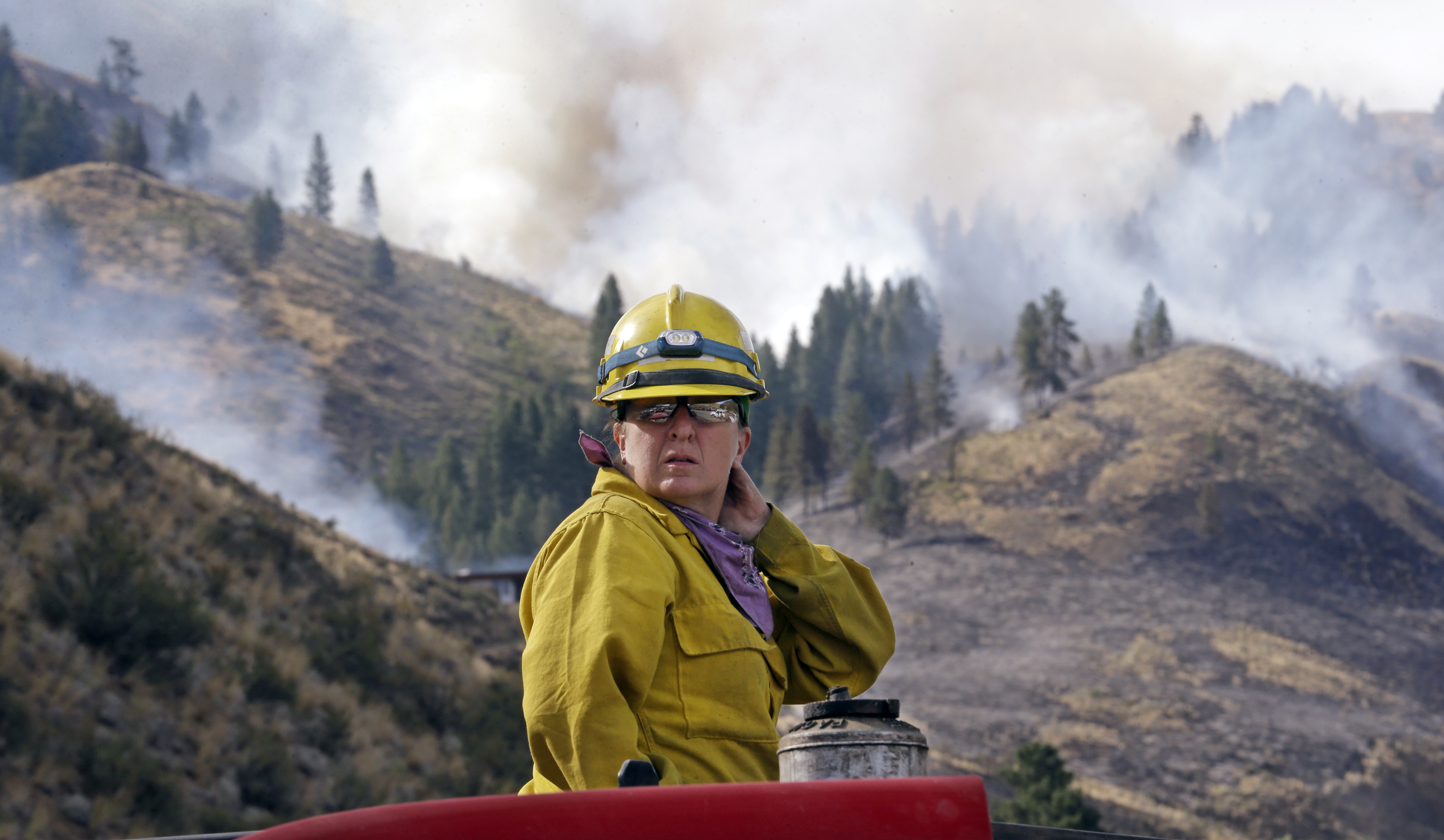 Firefighter Kathleen Calvin looks around as she sits atop her fire truck while waiting to begin work as smoke from a wildfire fills the sky behind Saturday, July 19, 2014, in Winthrop, Wash. (AP Photo/Elaine Thompson)