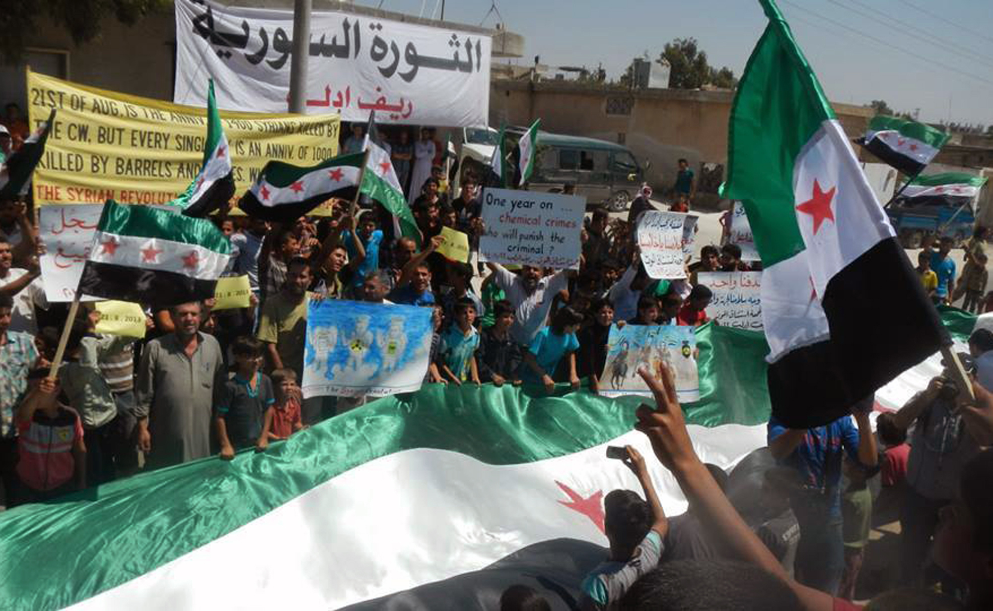 Anti-Syrian government protesters carry banners and a giant Syrian revolution flag during a demonstration in Idlib province, northern Syria. (Associated Press)