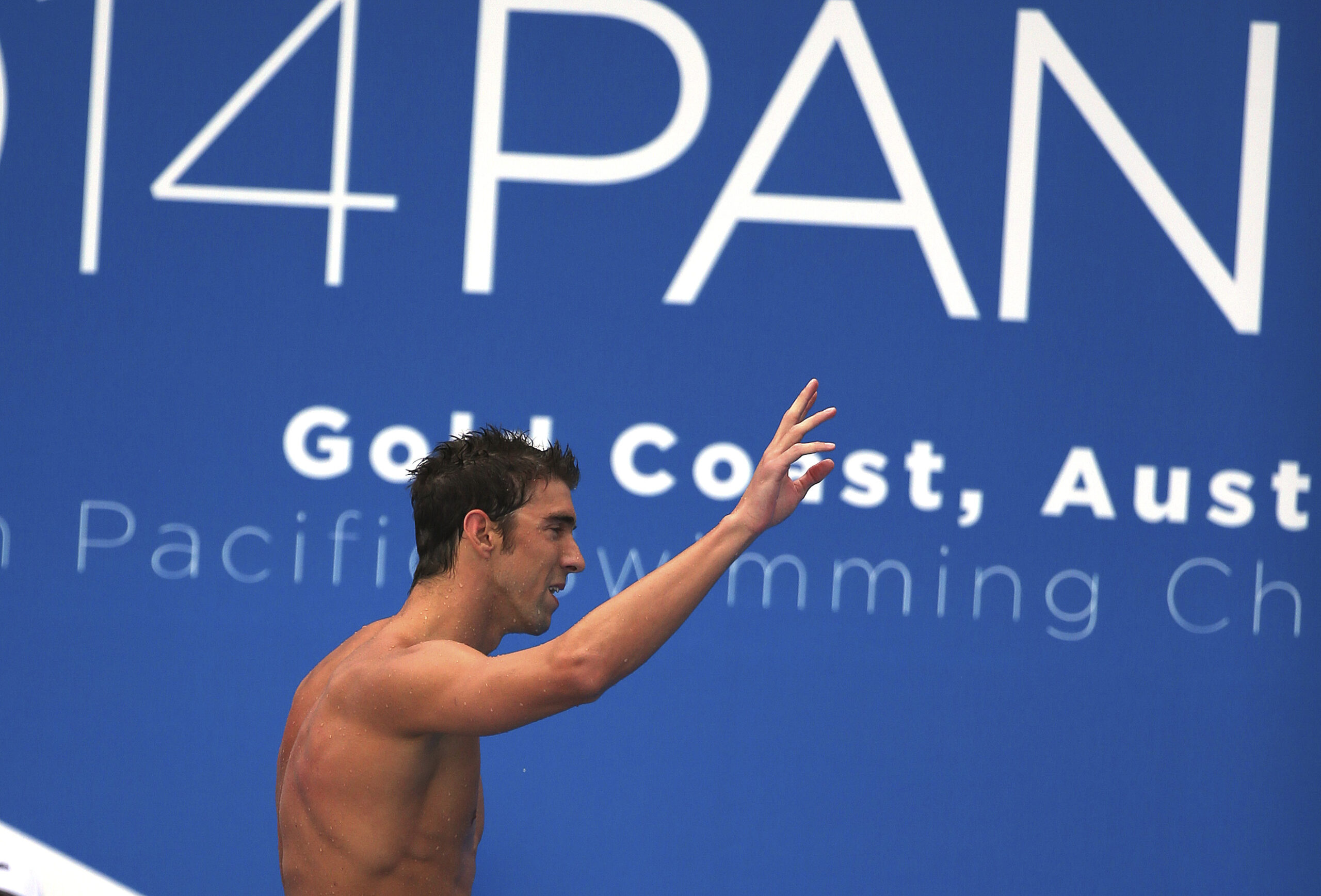 Michael Phelps of the U.S. waves as he leaves the pool deck after his men's 100m freestyle heat at the Pan Pacific swimming championships in Gold Coast, Australia, Friday, Aug. 22, 2014. (AP Photo/Rick Rycroft) (Rick Rycroft)