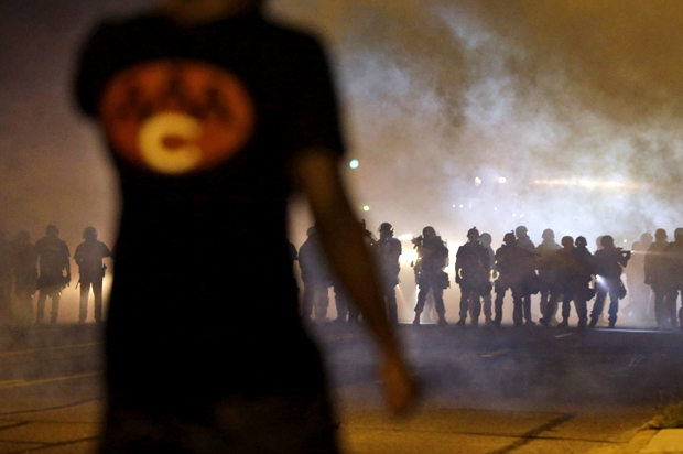 A man watches as police walk through a cloud of smoke during a clash with protesters, Aug. 13, 2014, in Ferguson, Mo. (AP/Jeff Roberson)