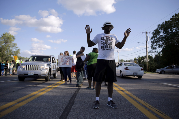 Kenan Morrison stands with his arms raised in the middle of a street, near other protesters, Aug. 12, 2014, in Ferguson, Mo. (AP/Jeff Roberson)