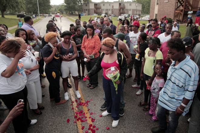 Lesley McSpadden, center, drops rose petals on the blood stains from her 18-year-old son Michael Brown who was shot and killed by police in the middle of the street in Ferguson, Mo., near St. Louis on Saturday, Aug. 9, 2014 (AP Photo/St. Louis Post-Dispatch, Huy Mach)