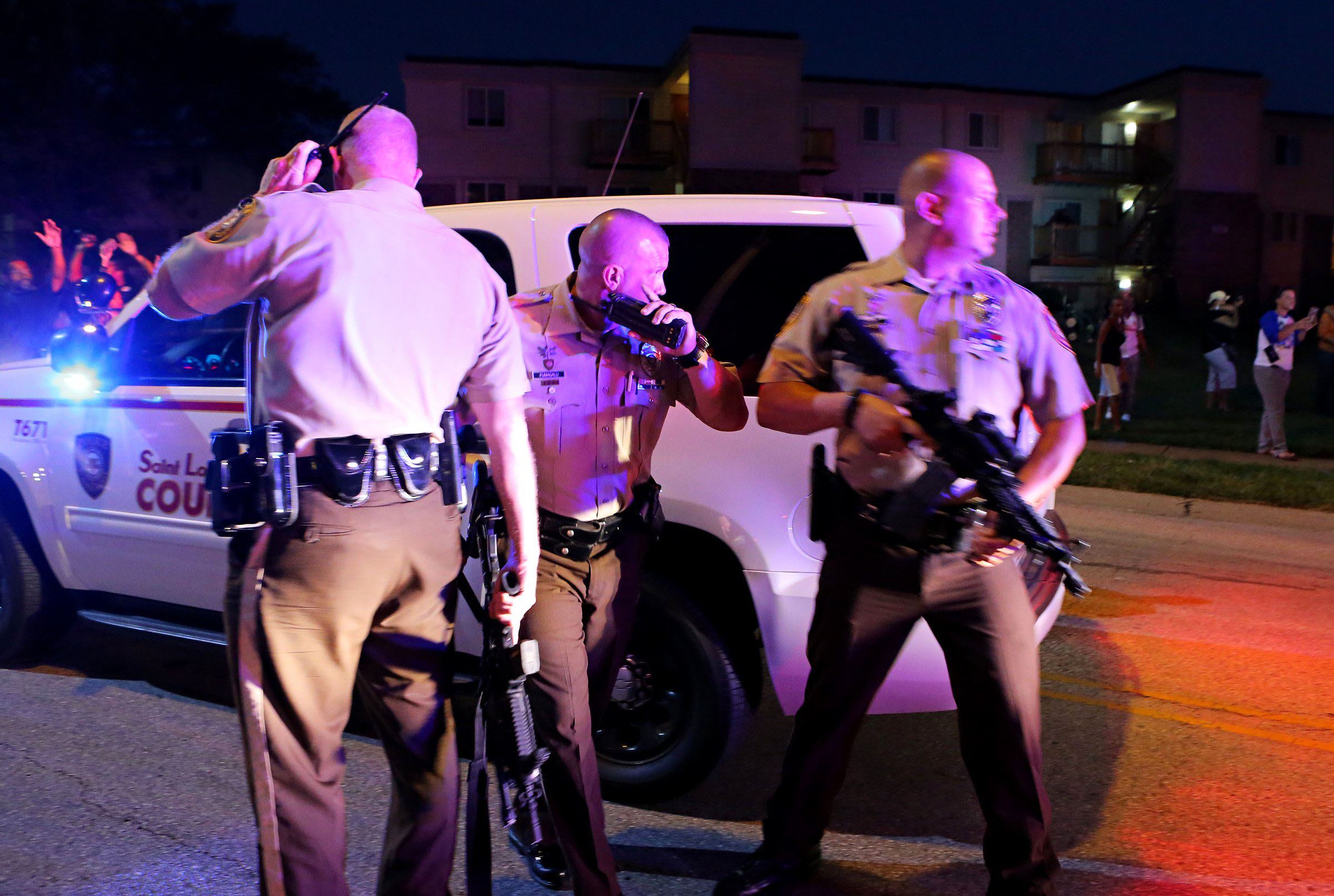 Police officers stand near a crowd that is gathering by the scene where 18-year-old Michael Brown was fatally shot by police in Ferguson, Mo., near St. Louis on Aug. 9, 2014. (AP Photo/St. Louis Post-Dispatch, David Carson)