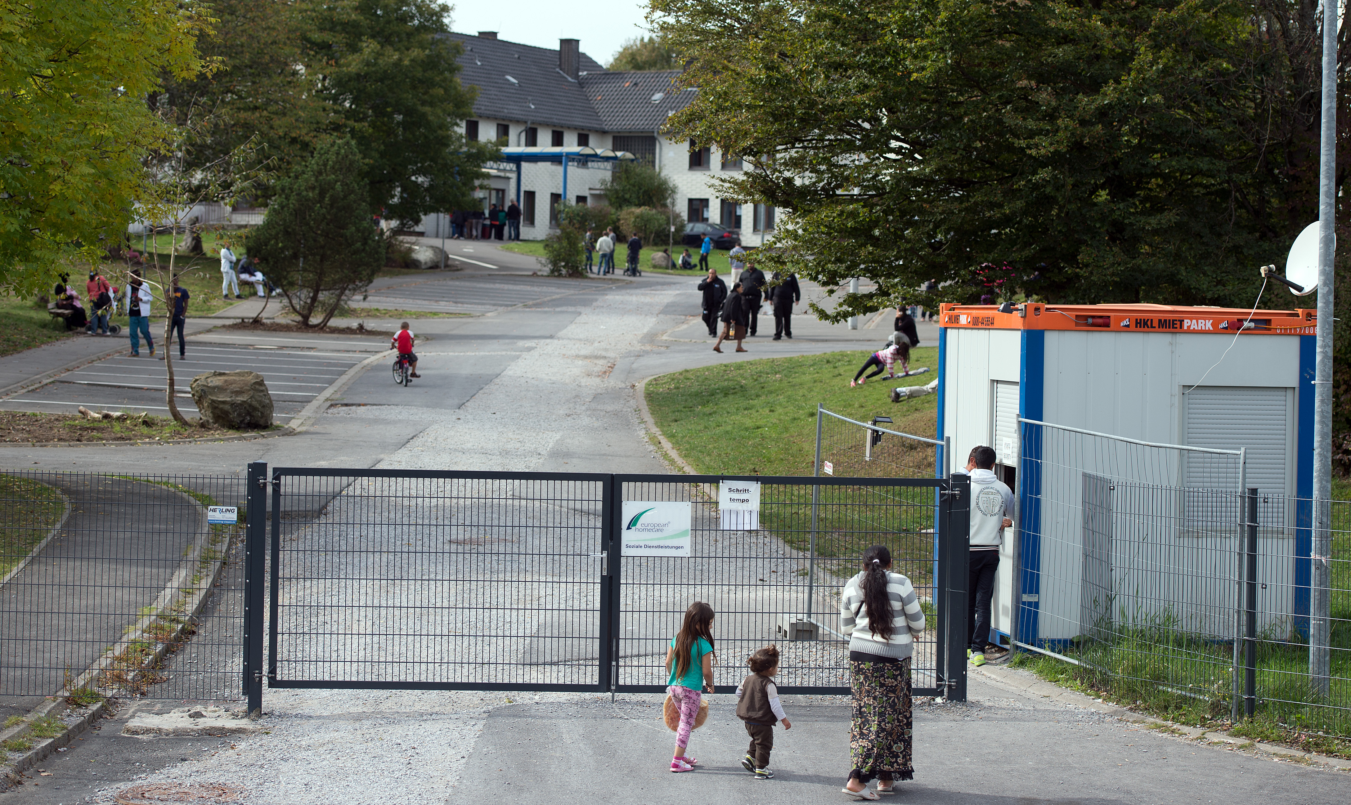 People walk in front of the entrance of the refugee camp in Burbach, Germany, Sunday Sept.28,2014.  Police are investigating accusations that guards at an asylum center in Burbach in western Germany repeatedly abused refugees physically and mentally. A police spokesman from Hagen near Burbach said Sunday that police raided the center and questioned both security guards and refugees after a local journalist received a DVD showing the abuse of an asylum seeker by guards. (AP Photo/dpa/Federico Gambarini) (AP)