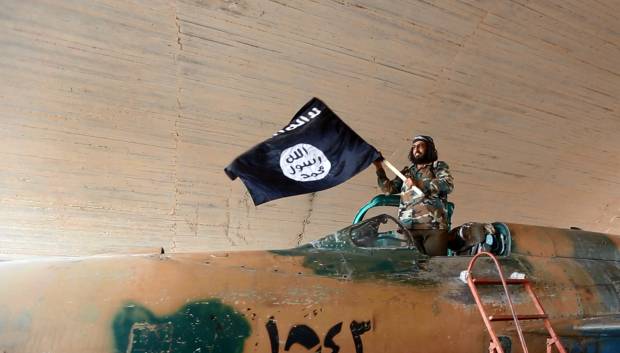 A fighter of the Islamic State group waves ISIS' flag from inside a captured government fighter jet following the battle for the Tabqa air base, in Raqqa, Syria on Sunday (AP Photo/ Raqqa Media Center of the Islamic State group)