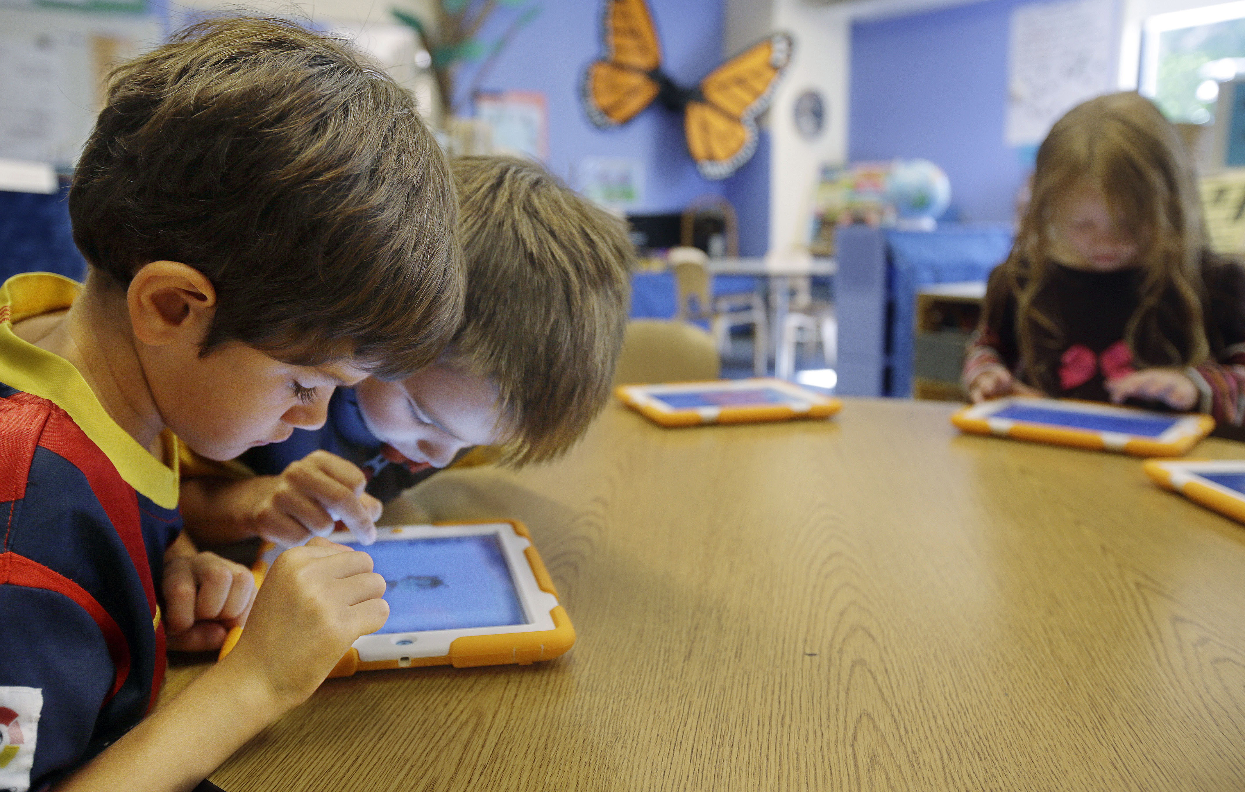 In this Thursday, Sept. 18, 2014 photo, Aiden Crott, 7, center, helps Daniel Hernadez, 5, with his ScratchJr iPad program while Talia Levitt, 7, right, works with hers at the Eliot-Pearson Children's School in Medford, Mass. Researchers created the app that teaches basic computer programming to kindergartners. (AP Photo/Stephan Savoia)