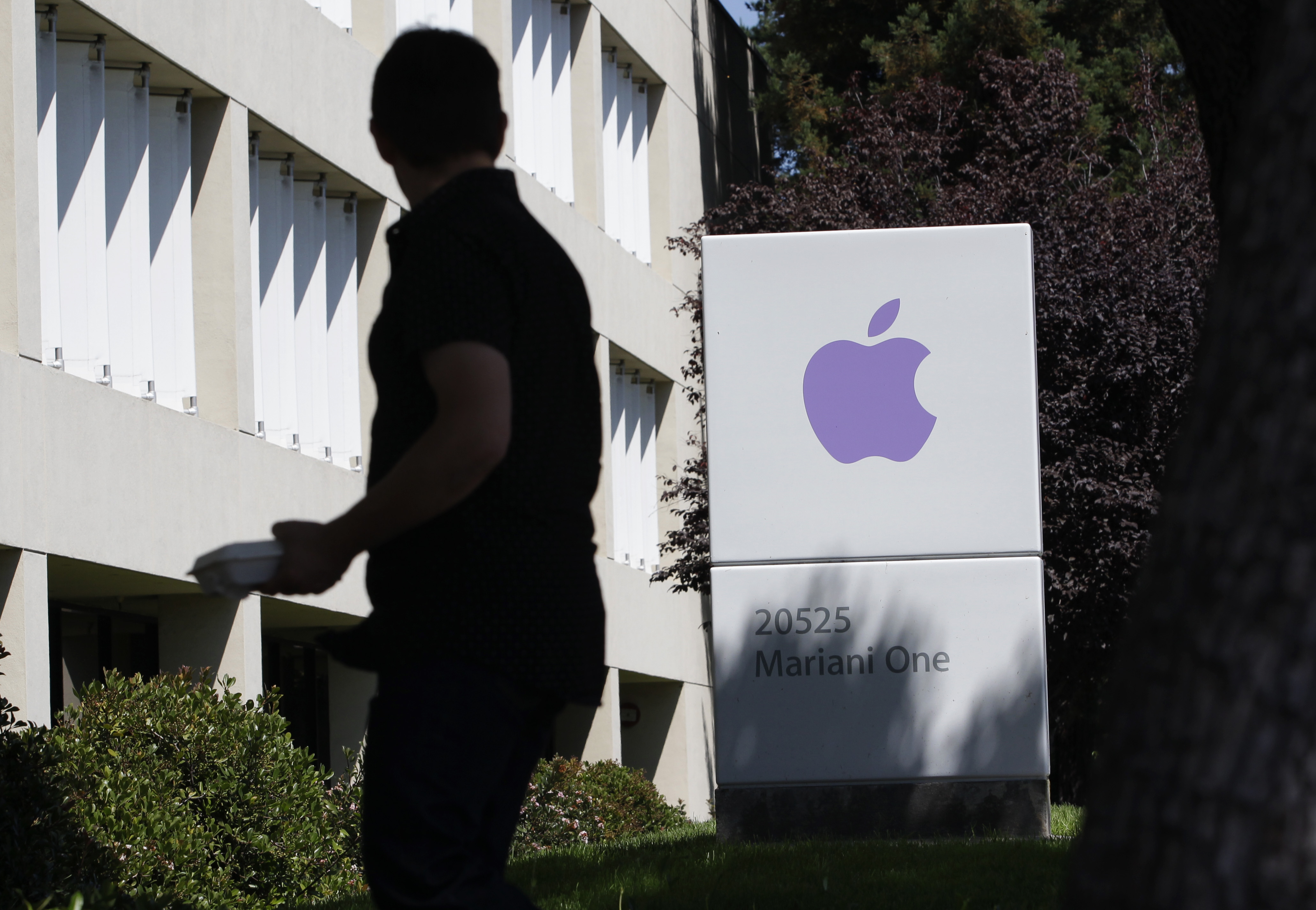 FILE - In this Aug. 25, 2011 file photo, an Apple employee walks between Apple buildings at Apple headquarters in Cupertino, Calif. Facebook and Apple, long known for cushy perks such as free meals, laundry service and massages, are among some of Silicon Valley's biggest companies. (AP Photo/Paul Sakuma, File) (AP)