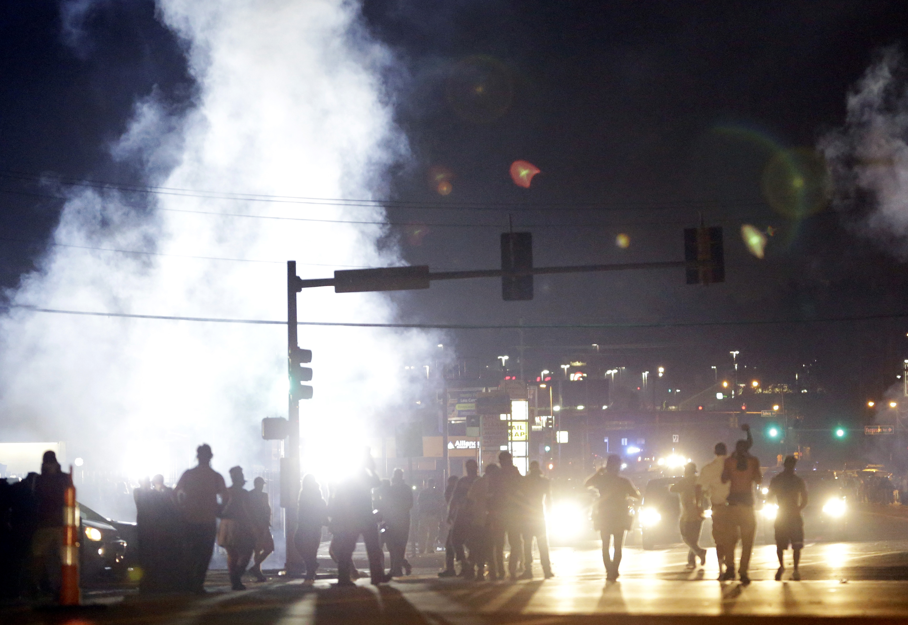 In this Monday, Aug. 18, 2014 file photo, people stand near a cloud of tear gas in Ferguson, Mo. during protests for the Aug. 9 shooting of unarmed black 18-year-old Michael Brown by a white police officer. The U.S. government agreed to a police request to shut down several miles of airspace surrounding Ferguson, even though authorities said their purpose was to keep media helicopters away during protests in August, according to recordings of air traffic control conversations obtained by The Associated Press. (AP Photo/Jeff Roberson)