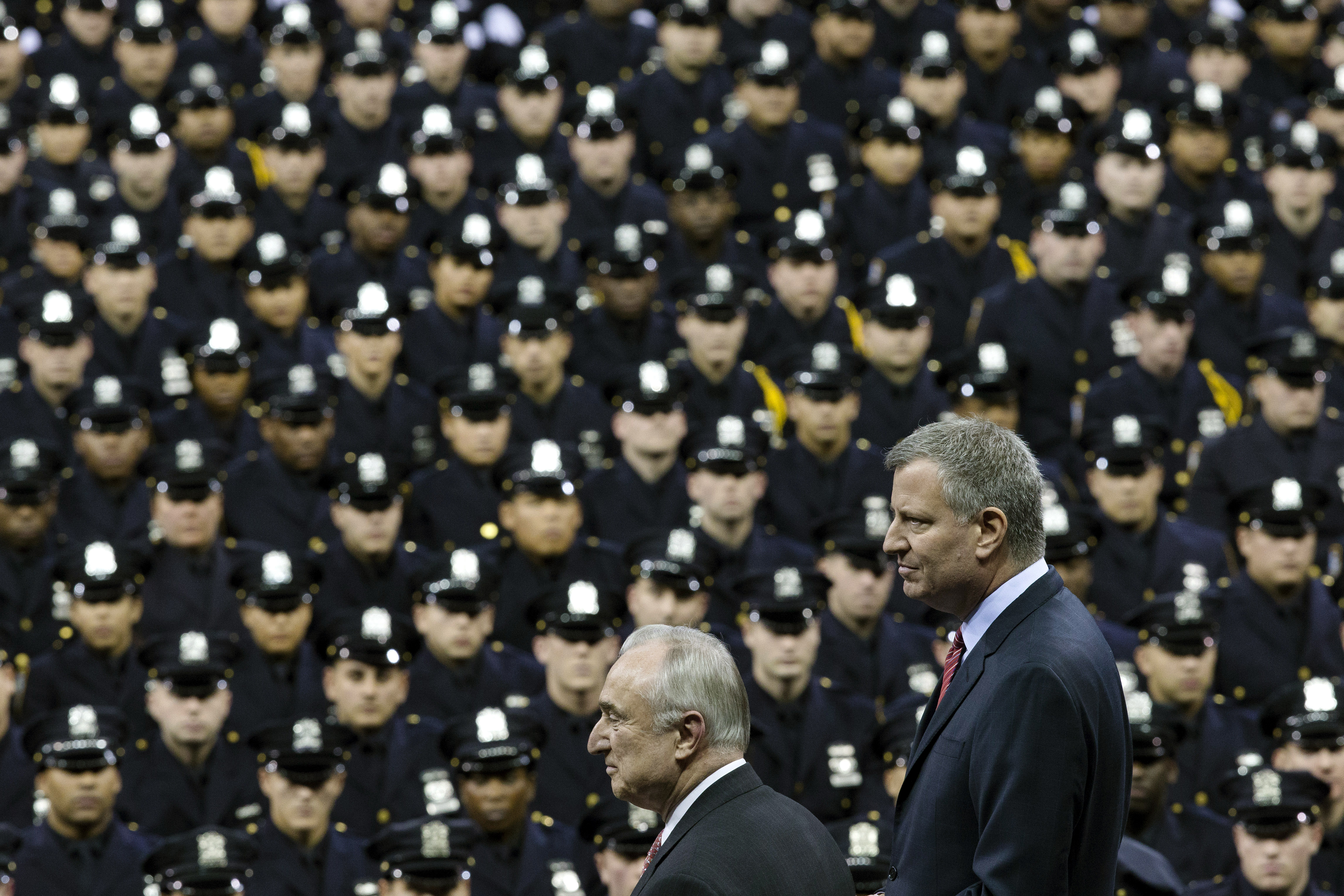FILE - In this Monday, Dec. 29, 2014 file photo New York City Mayor Bill de Blasio, right, and NYPD police commissioner Bill Bratton, center, stand on stage during a New York Police Academy graduation ceremony at Madison Square Garden in New York. (AP/John Minchillo)
