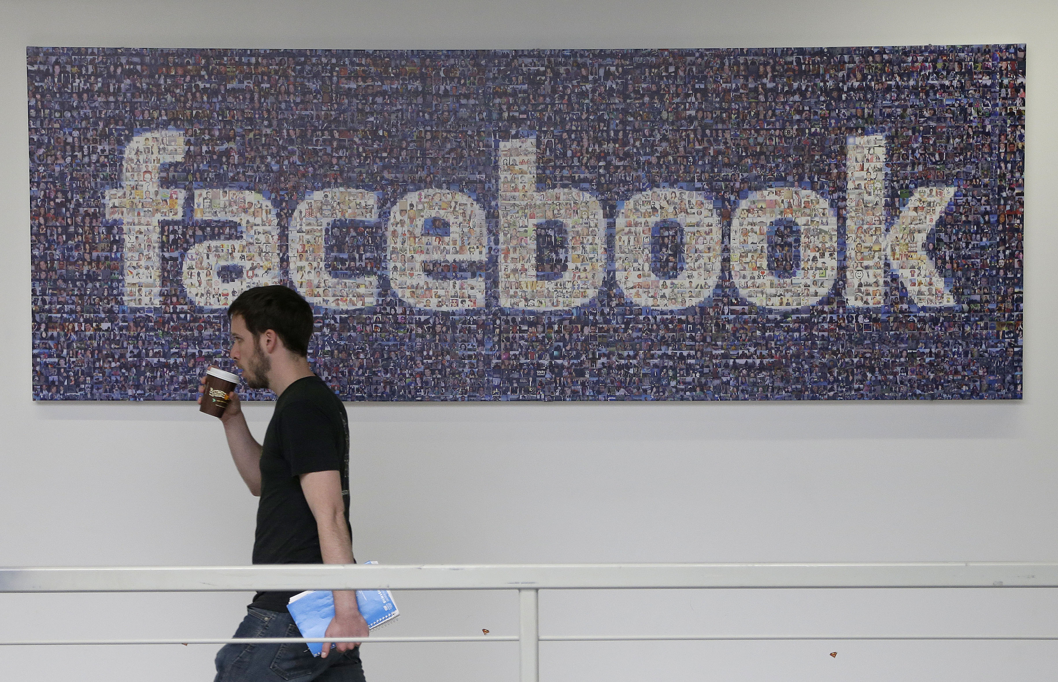 FILE - In this March 15, 2013, file photo, a Facebook employee walks past a sign at Facebook headquarters in Menlo Park, Calif. (AP/Jeff Chiu)