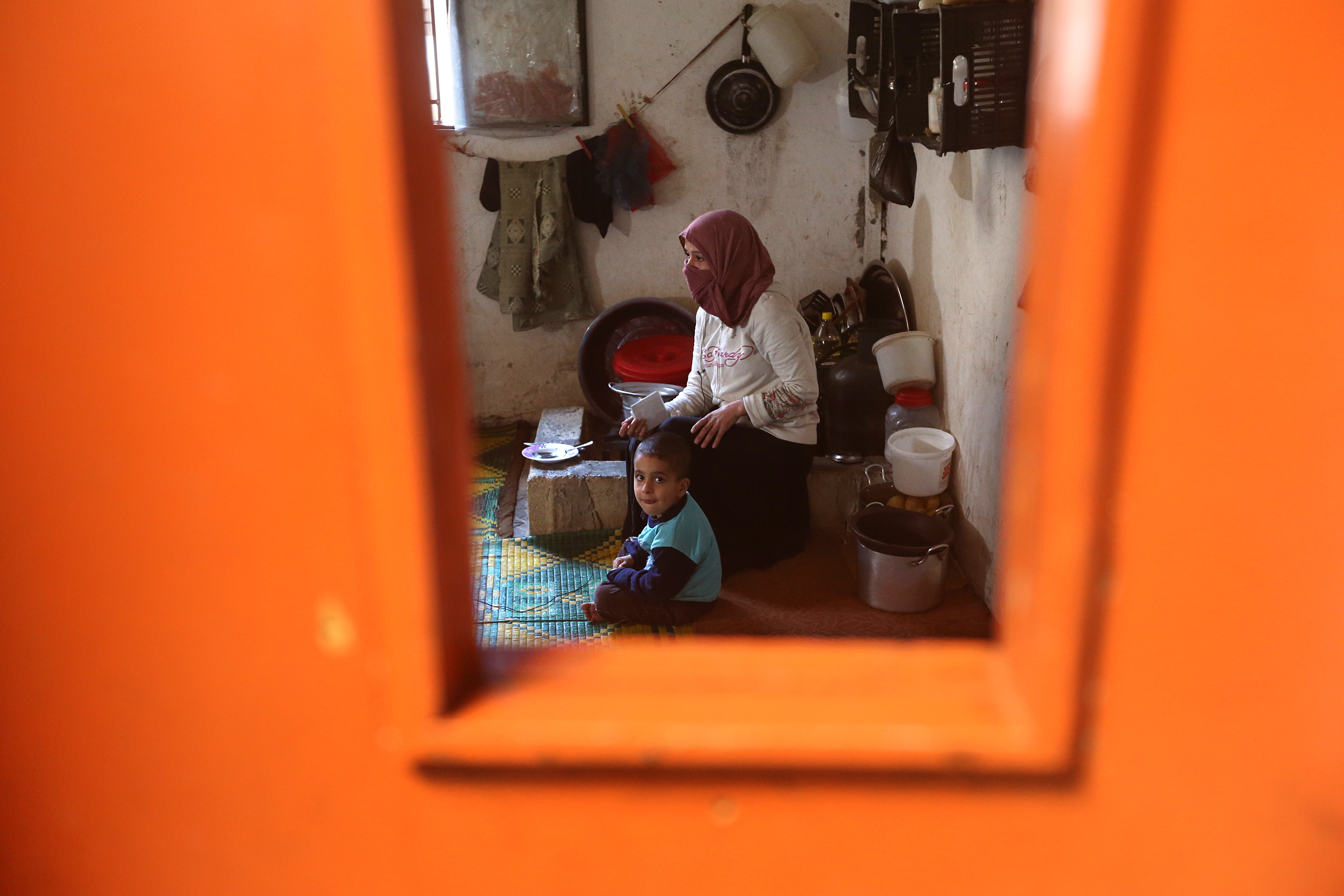 In this photo taken Friday, March 6, 2015, Syrian refugee woman Amani Abdul-Qadir, 27, is seen through a broken window of the door as she sits next to her son Hozeifar, 5, inside her room that used to be a classroom at the Al-Rama Public School that has become home to 22 Syrian families at the Lebanese-Syrian border village of al-Rama, north Lebanon. "Our life here is appalling," Amani said, referring to the poverty life they live, relying on money and food offered by the U.N. and humanitarian organizations. (AP Photo/Hussein Malla) (AP)