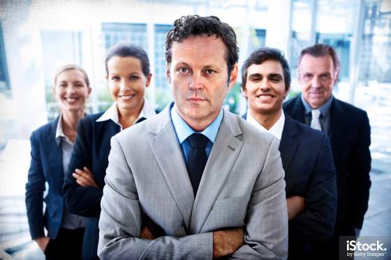 Portrait of a handsome business leader crossing his arms with his team standing behind him