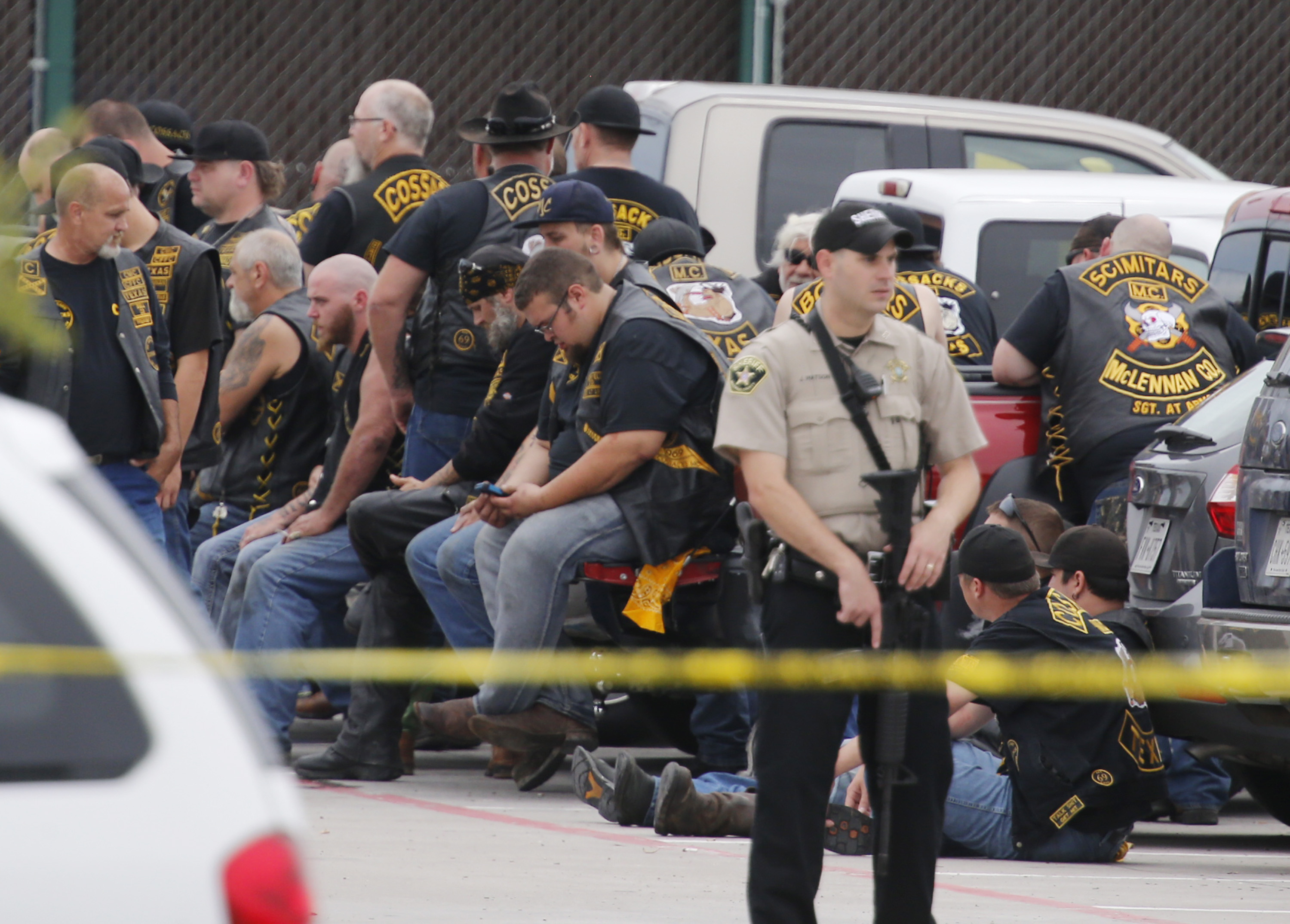 A McLennan County deputy stands guard near a group of bikers in the parking lot of a Twin Peaks restaurant Sunday, May 17, 2015, in Waco, Texas. Waco Police Sgt. W. Patrick Swanton told KWTX-TV there were "multiple victims" after gunfire erupted between rival biker gangs at the restaurant. (Rod Aydelotte/Waco Tribune-Herald via AP) (AP)