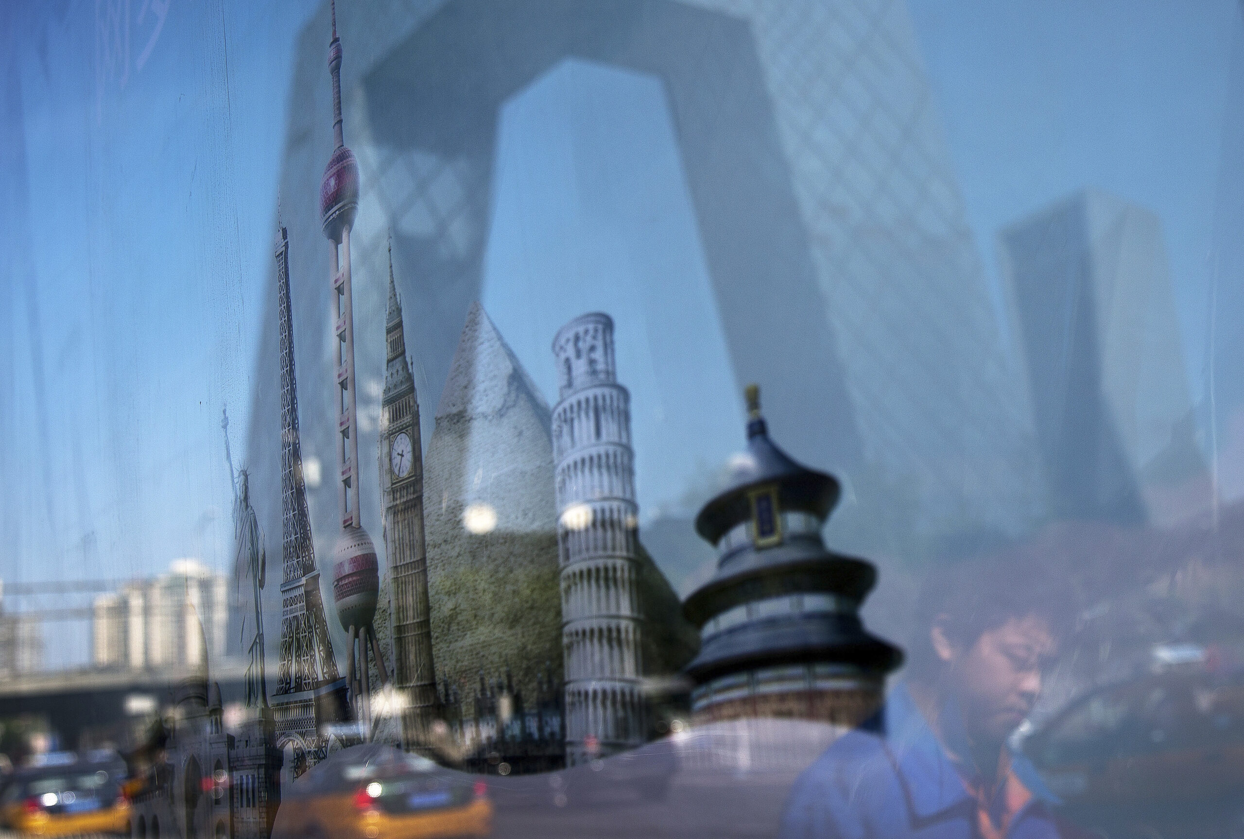 A man and the building of China Central Television (CCTV) headquarters is reflected on an advertisement billboard shows various countries' scenic places on display at the Central Business District of Beijing, China Wednesday, May 20, 2015. If the U.S. doesn't write the rules of international trade, President Barack Obama warns, China will. In fact, China is already helping write those rules, and in some ways has jumped ahead of the game. (AP Photo/Andy Wong) (Andy Wong)
