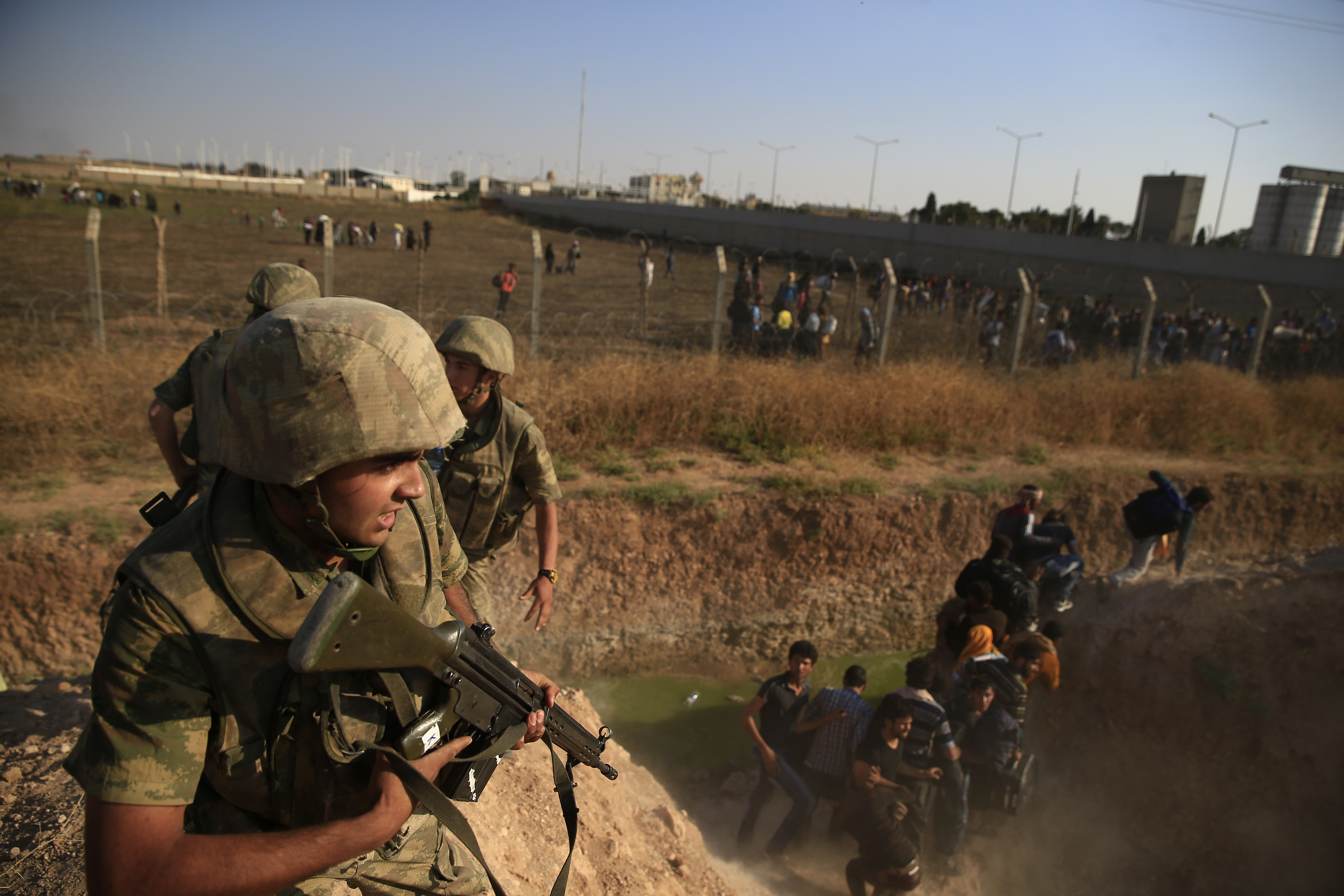 Turkish soldiers run to control Syrian refugees crossing into Turkey from Syria after breaking the border fence, background, in Akcakale, Sanliurfa province, southeastern Turkey,  Sunday, June 14, 2015. Thousands of Syrians cut through a border fence and crossed over into Turkey on Sunday, fleeing intense fighting in northern Syria between Kurdish fighters and jihadis.The flow of refugees came as Syrian Kurdish fighters closed in on the outskirts of a strategic Islamic State-held town on the Turkish border. (AP Photo/Lefteris Pitarakis) (AP)