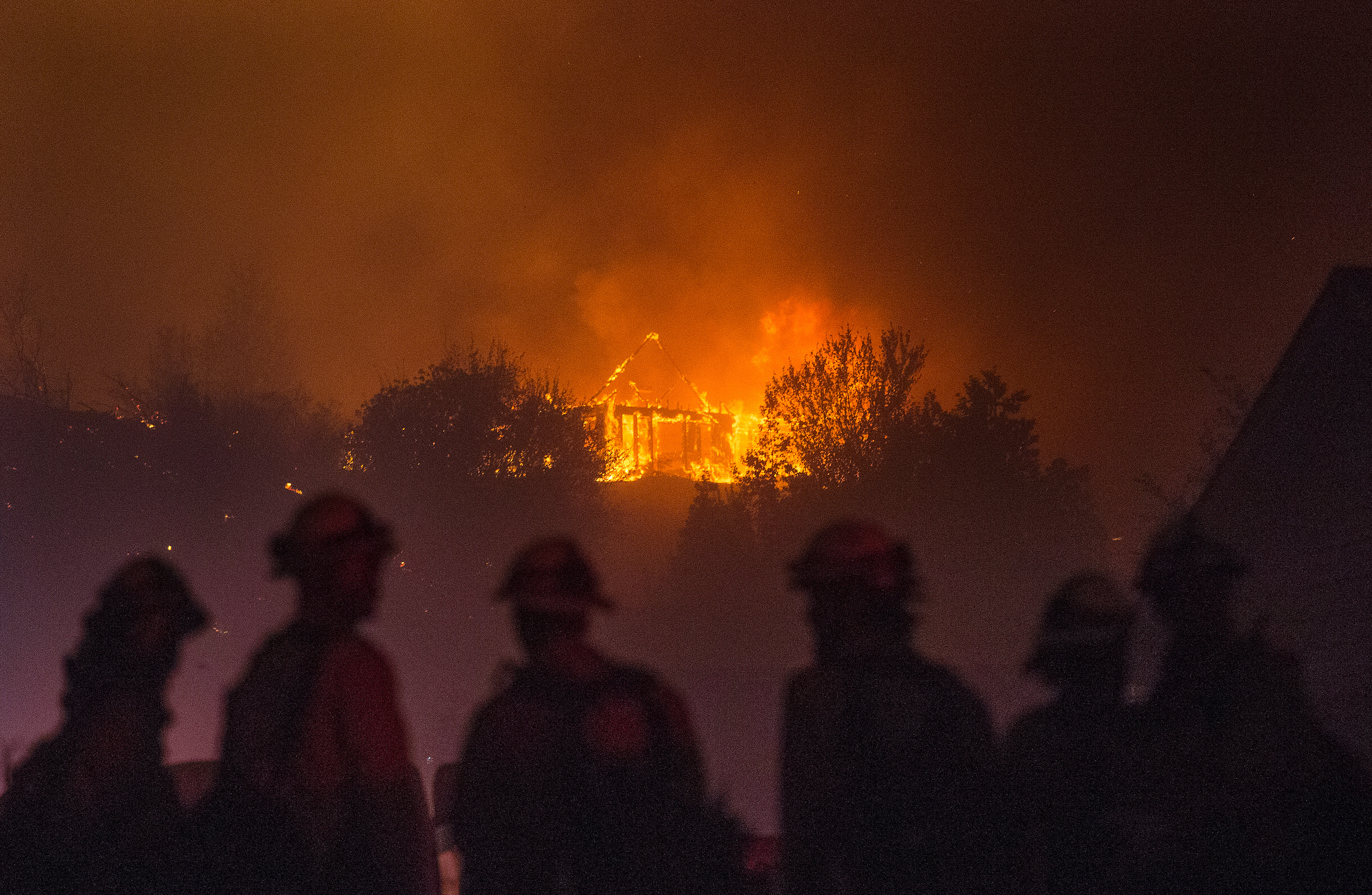 In this Sunday, June 28, 2015 photo provided by The Wenatchee World, Forest Service fire fighters from Leavenworth  watch as a house burns in northern Wenatchee, Wash. A wildfire fueled by high temperatures and strong winds roared into a central Washington neighborhood, destroying properties and forcing residents of several hundred homes to flee, authorities said Monday. (Don Seabrook/The Wenatchee World via AP) (AP)