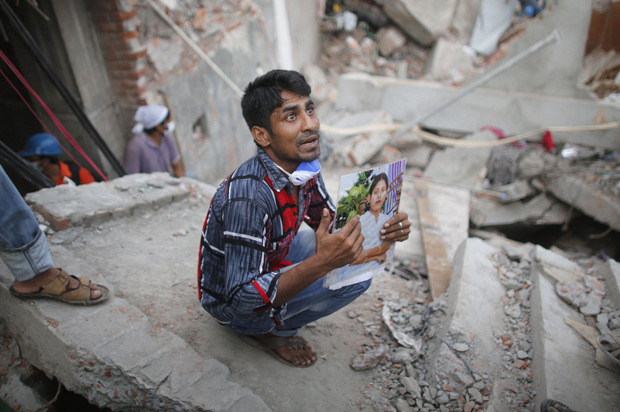 A relative holds up a picture of a garment worker in front of the rubble of the collapsed Rana Plaza building, in Savar, April 27, 2013. (Reuters/Andrew Biraj)