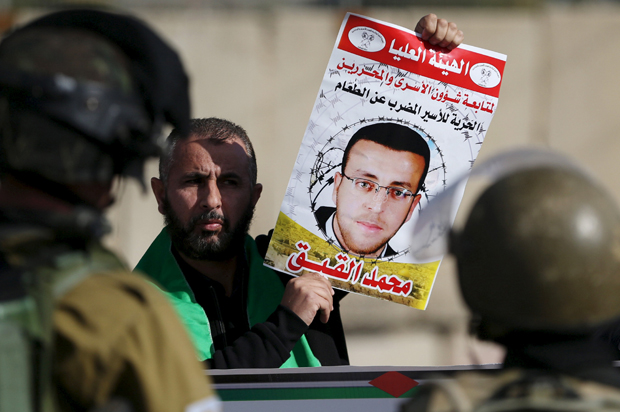 A Palestinian protester standing in front of Israeli soldiers holds the picture of imprisoned journalist Mohammad al-Qiq, near the occupied West Bank city of Ramallah on Jan. 22, 2016. (Reuters/Mohamad Torokman)