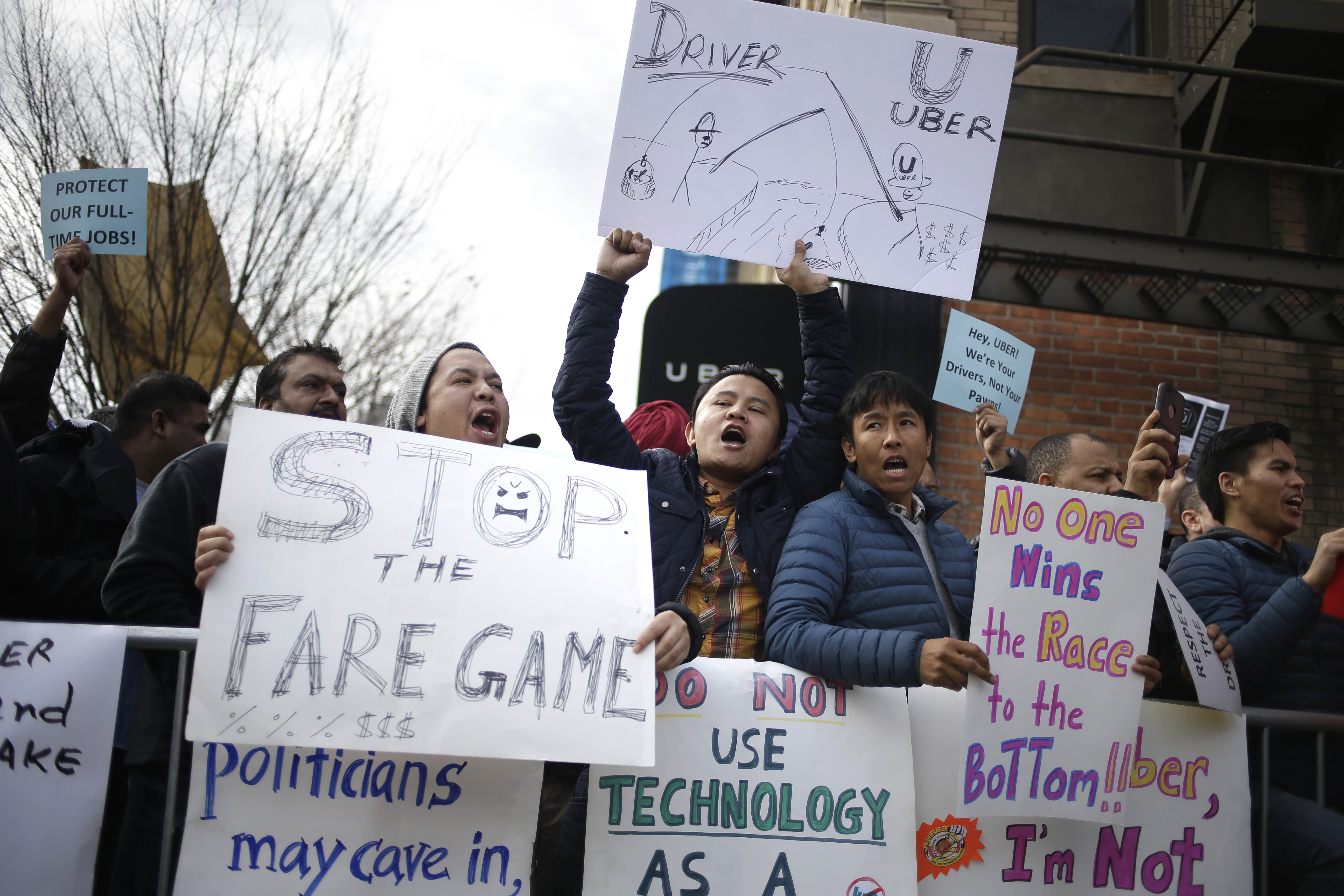 Uber drivers and their supporters hold signs and chant during a rally at an Uber office in New York in February (AP)