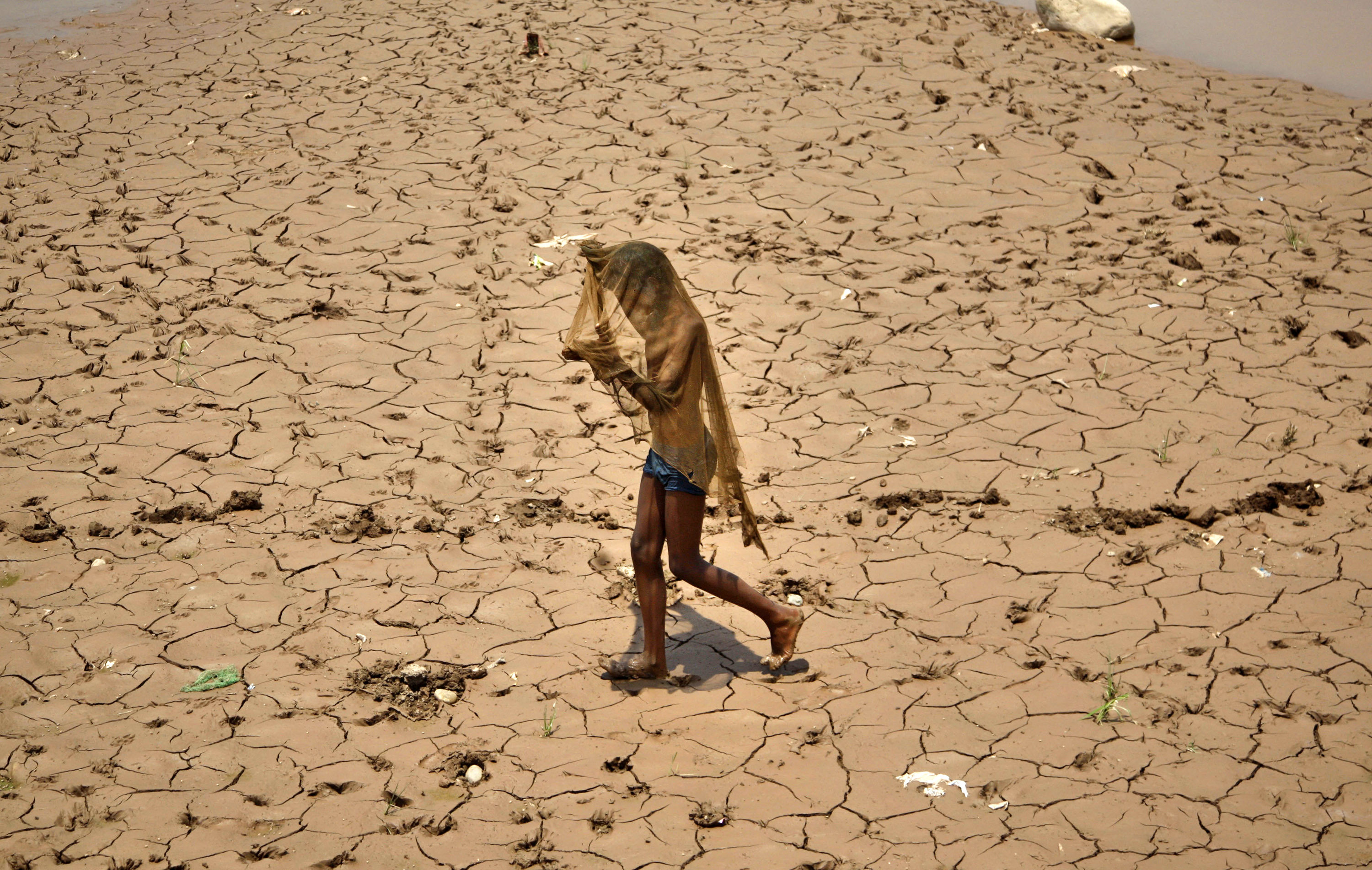 FILE - In this Saturday, June 1, 2013, file photo, a young Indian covers his face to protect from the heat as he walks on a dried bed of the River Tawi on a hot summer day in Jammu, India. India is launching programs to protect people from extreme heat in two high-risk cities, after a devastating heat wave killed at least 2,500 people across the country last year. (AP Photo/Channi Anand, file)