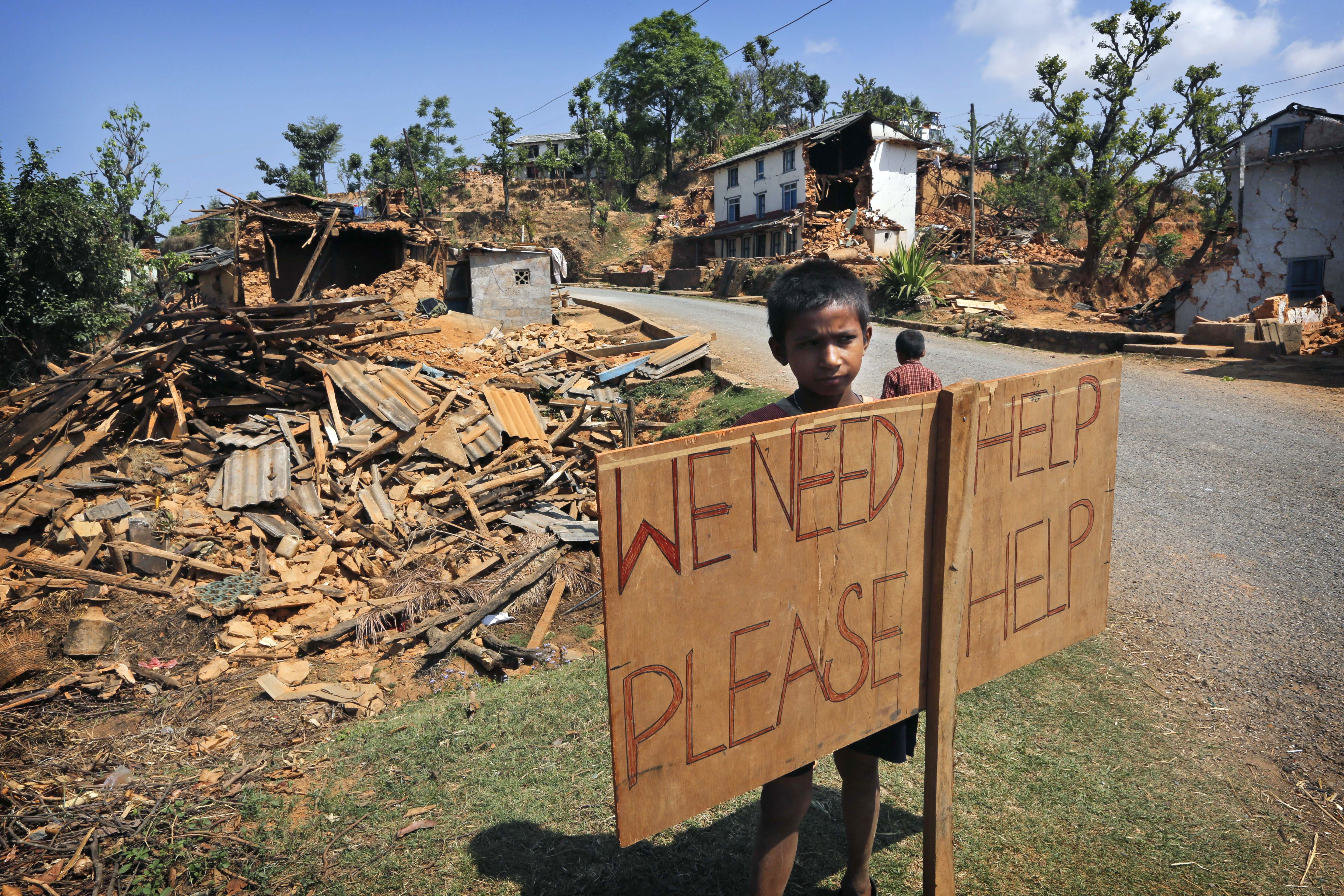 FILE - In this May 2, 2015 file photo, a Nepalese boy stands outside his village with a signboard asking for help in Pauwathok village, Sindhupalchok district, Nepal. A year after a set of devastating earthquakes plunged Nepal into chaos and economic decline, one question remains on everyones mind: what if it happens again? Scientists have been warning Nepal and other Himalayan countries for years that quake risks in the region are high. But while citizens are preparing for the worst by building sturdier homes and stockpiling emergency supplies, experts say officials still have a long way to go in preparing for possible, if not probable, disaster. (AP Photo/Manish Swarup, File) (AP)
