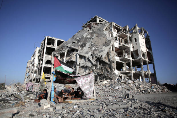 Palestinians sit next to their demolished home, in the town of Beit Lahiya, northern Gaza, on Aug. 11, 2014 (AP/Khalil Hamra)