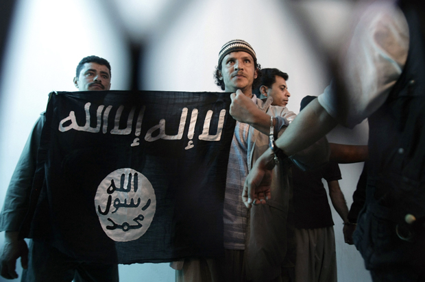 A suspected Yemeni al-Qaida militant, center, holds an Islamist banner as he stands behind bars during a court hearing in state security court in Sanaa, Yemen, April 23, 2013. (AP/Hani Mohammed)