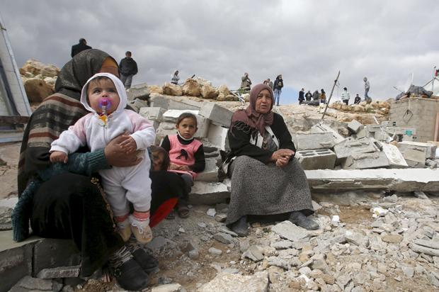 Palestinians sit among the rubble of their house, which was demolished by Israeli bulldozers, in the West Bank village of Jimba, February 2, 2016. (Reuters/Mussa Qawasma)