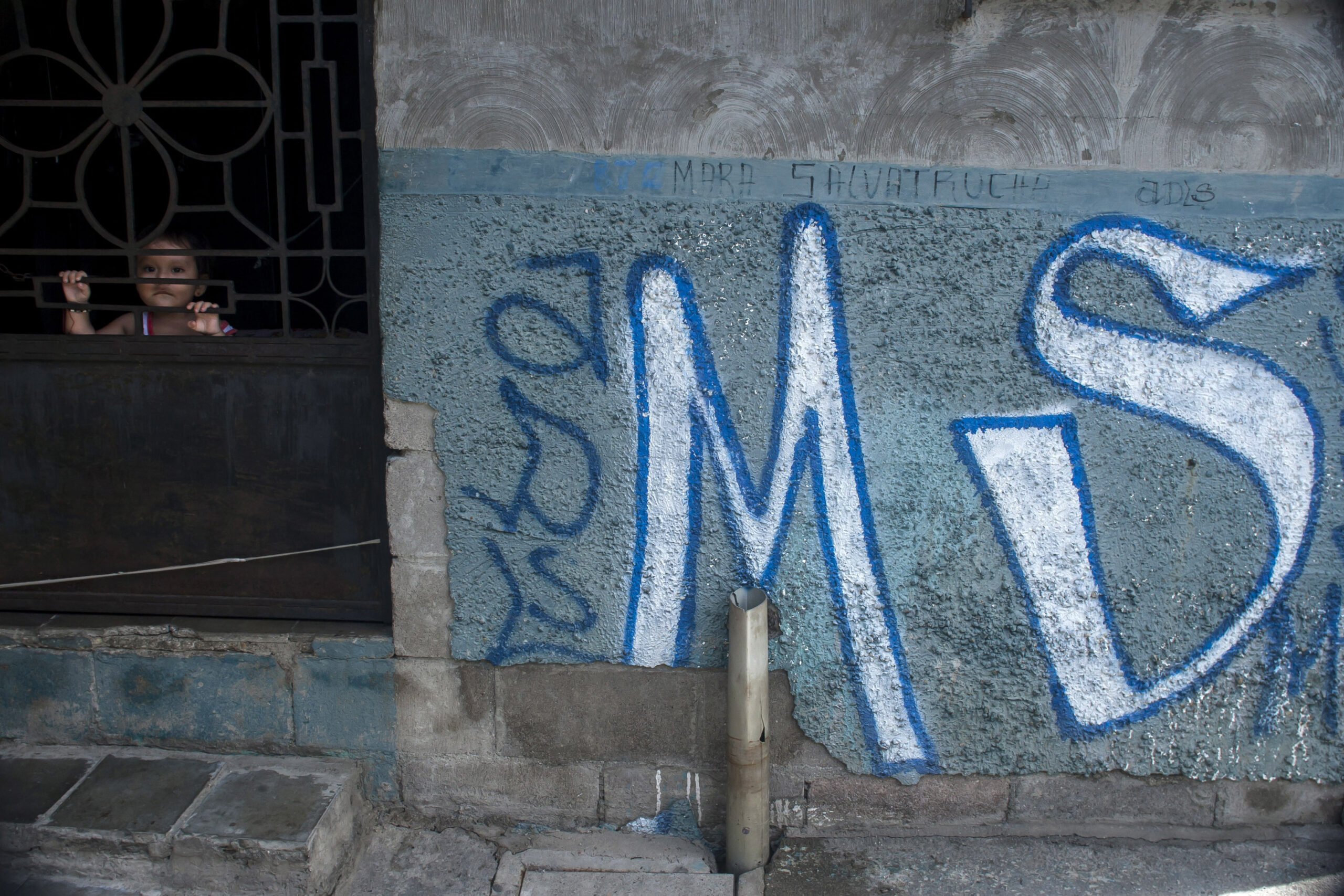 In this June 21, 2016 photo, a child peers from behind the door of her home, covered with Mara Salvatrucha gang graffiti, in Soyapango, El Salvador. After becoming the world's murder capital last year and posting an equally bloody start to 2016, El Salvador has seen its monthly homicide rates fall by about half. The government attributes the drop to a tough military crackdown on the country's powerful gangs, while the gangs themselves claim credit for a nonaggression pact between the three biggest criminal groups. (AP Photo/Salvador Melendez) (AP)