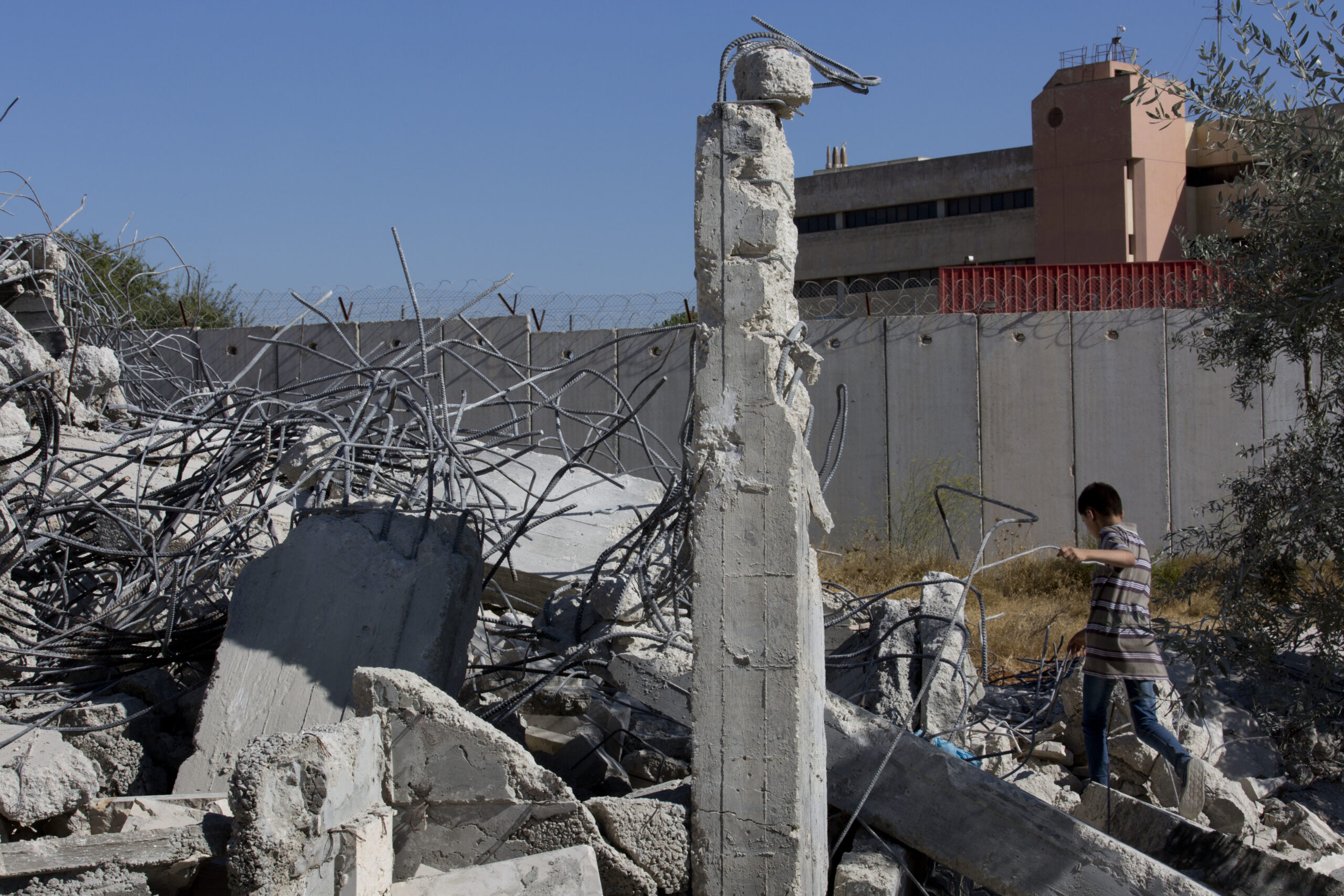 A Palestinian boy walks over the rubble of a house that overlooks the Israeli separation barrier, background, and was demolished by the Israeli army, in the West Bank village of Qalandia, near Ramallah, Tuesday, July 26, 2016. (AP)