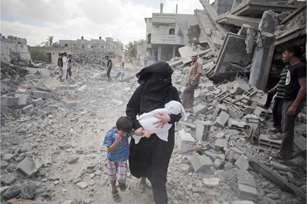 A Palestinian woman passes by rescuers inspecting the rubble of destroyed houses following Israeli strikes in Rafah refugee camp, southern Gaza Strip. (AP/Khalil Hamra)