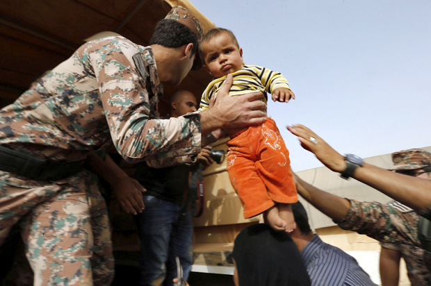 A Jordanian soldier carries a Syrian refugee child to help him board a Jordanian army vehicle with his family near Ruwaished, Jordan, September 10, 2015. (Reuters/Muhammad Hamed)
