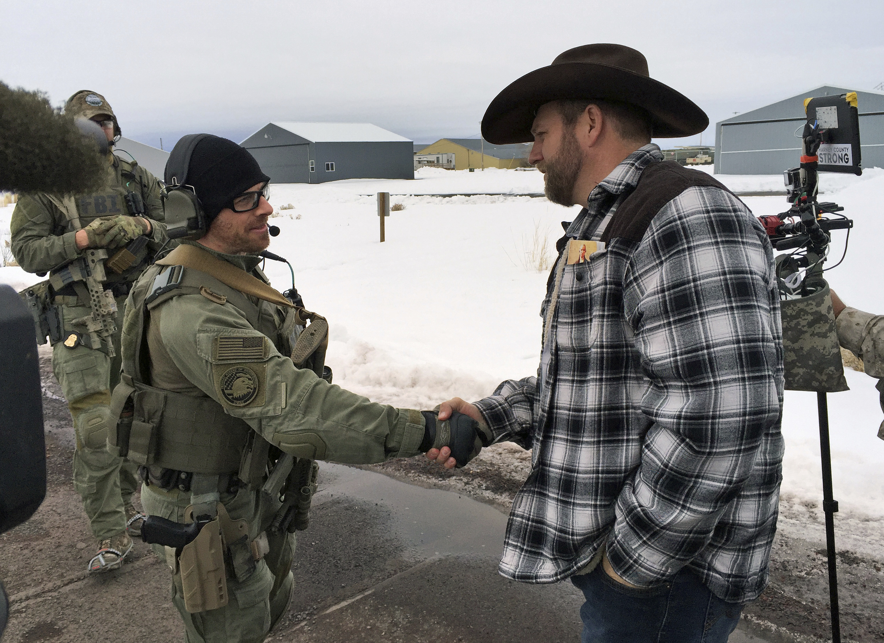 FILE - In this Jan. 22, 2016, file photo, Ammon Bundy, right, shakes hand with a federal agent guarding the gate at the Burns Municipal Airport in Burns, Ore. Bundy, the leader of a federal wildlife refuge takeover in Oregon says his group will "continue to stand" after he and six others were acquitted last week in Portland, Ore., of charges in the case. Bundy remains in jail because he still faces charges in the 2014 standoff at his father's Nevada ranch. (AP Photo/Keith Ridler, File) (AP)