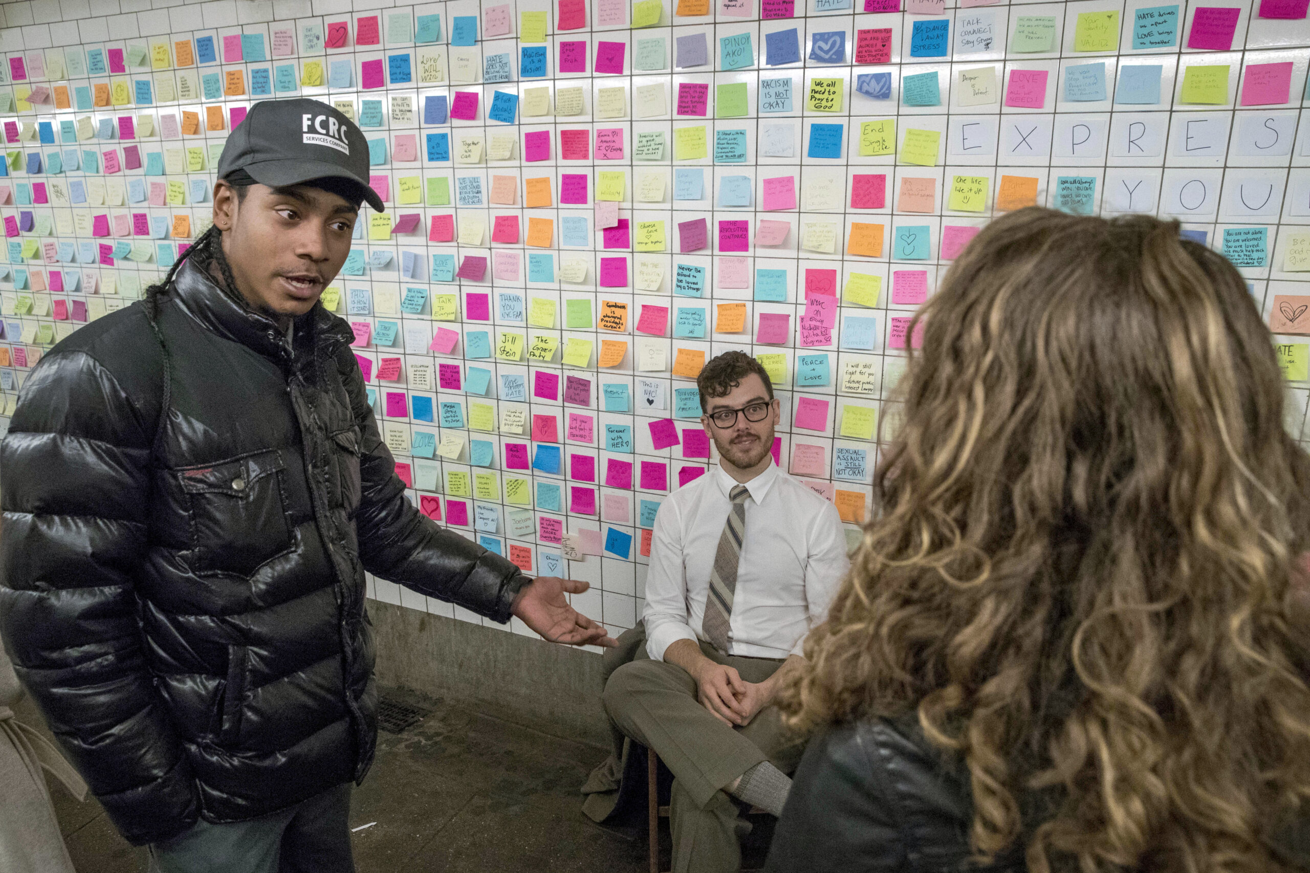 Matthew Chavez, center, who goes by the artist name Levee, talks to commuters about the messages posted on the "Subway Therapy" wall, Friday, Nov. 11, 2016, in New York. Levee started the installation in the underground passageway that connects the 1 train to the L train on 14th St., where people are encouraged to leave their feelings about the presidential election written on Post-It notes. (AP Photo/Mary Altaffer) (AP)