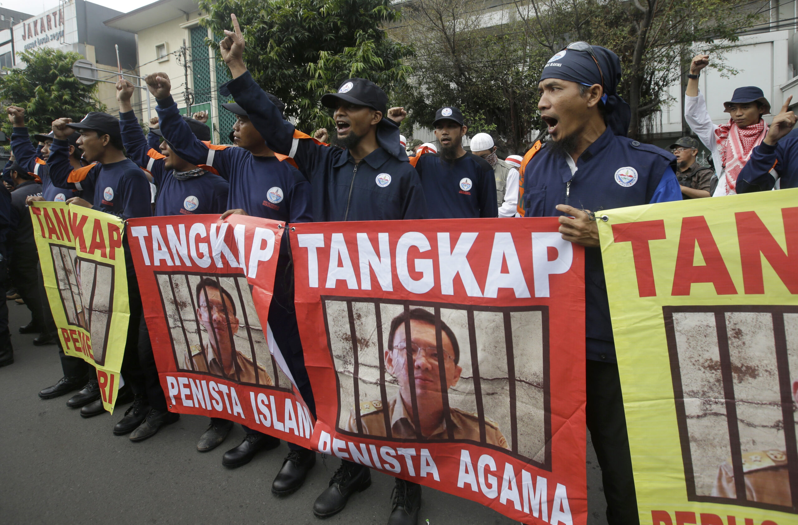 Protesters display posters of Jakarta Governor Basuki Tjahaja Purnama, popularly known as "Ahok," with writings that read: "Arrest blasphemer" during his trial hearing at a district court in Jakarta, Indonesia, Tuesday, Dec. 13, 2016. (AP Photo/Achmad Ibrahim)