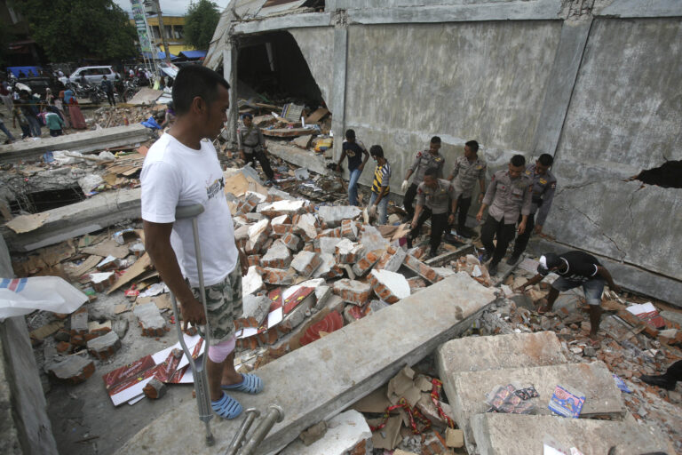 Faisal Marwan, left, who was injured in Wednesday's earthquake, stands on the ruins of his shop as police officers clear the rubble in Tringgading, Aceh province, Indonesia, Friday, Dec. 9, 2016. Over a hundred of people were killed in the quake that hit the northeast of the province on Sumatra before dawn Wednesday. Hundreds of people were injured and thousands buildings destroyed or heavily damaged. (AP Photo/Binsar Bakkara) (AP)
