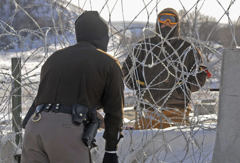 A law enforcement officer speaks to a protester against the Dakota Access Pipeline through a wall of razor wire on the Backwater Bridge over Cantapeta Creek on Thursday afternoon, Dec. 8, 2016. Protesters have been trespassing at the site and cutting wire in attempts to gain access to the pipeline work area in southern Morton County. (Tom Stromme/The Bismarck Tribune via AP) (AP)
