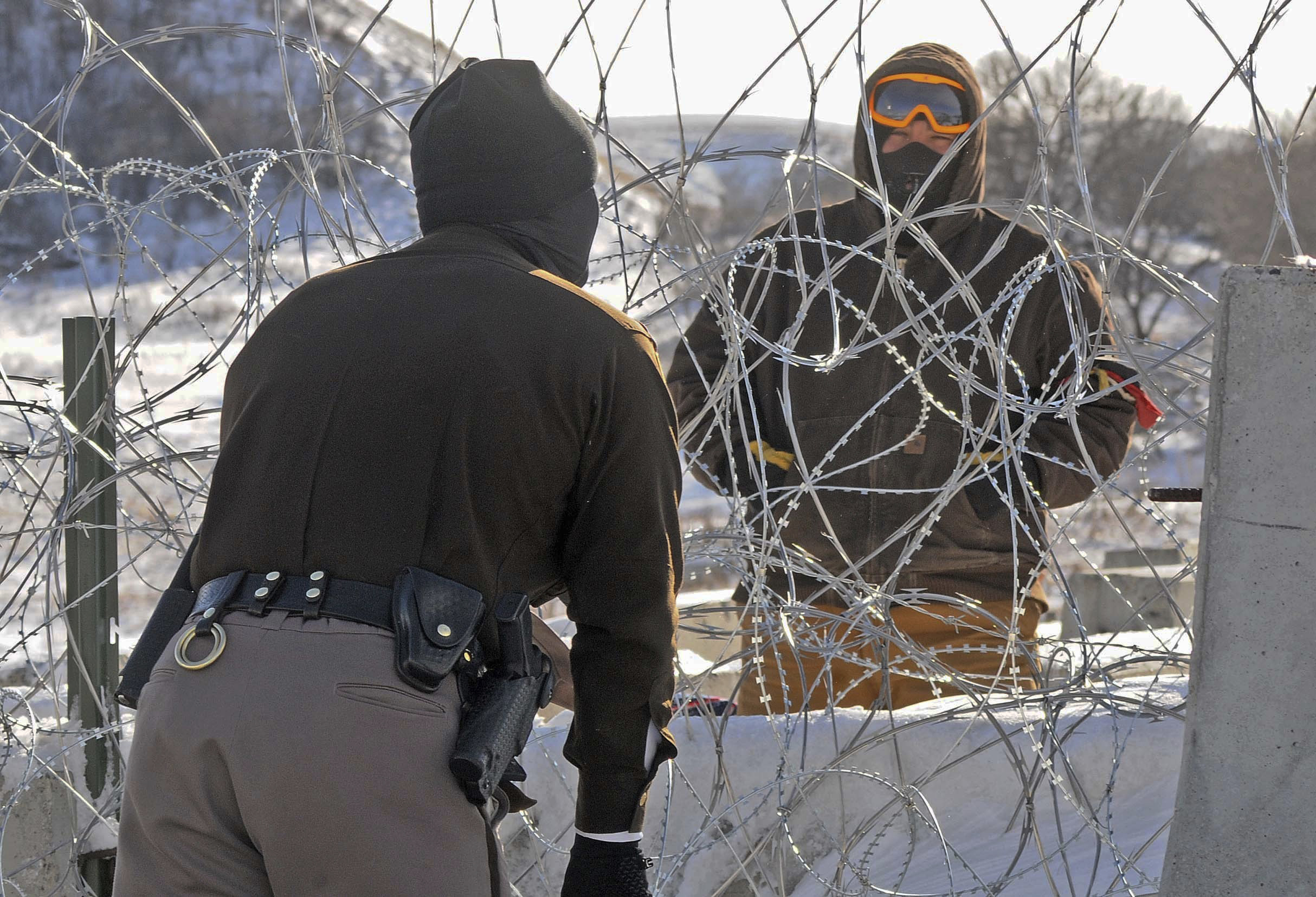 A law enforcement officer speaks to a protester against the Dakota Access Pipeline through a wall of razor wire on the Backwater Bridge over Cantapeta Creek on Thursday afternoon, Dec. 8, 2016. Protesters have been trespassing at the site and cutting wire in attempts to gain access to the pipeline work area in southern Morton County. (Tom Stromme/The Bismarck Tribune via AP) (AP)