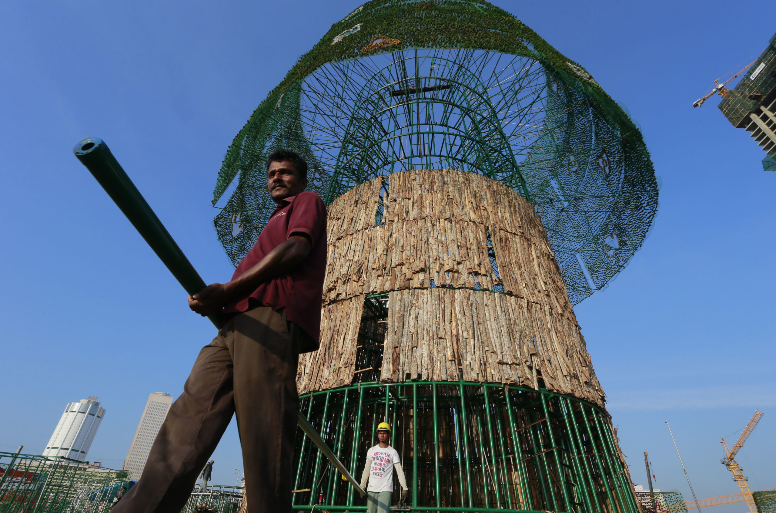 In this Thursday, Dec. 15, 2016 photo, Haloluwage Don Nanayakkara, left, carries a steel rod with another worker as they try to build an enormous, artificial Christmas tree on a popular beachside promenade in Colombo, Sri Lanka. The idea for the tree came from this Buddhist driver at Colombo’s port who makes decorations in his spare time. Hundreds of Sri Lanka’s port workers and volunteers are struggling to put up the towering Christmas tree in time for the holidays. The majority-Buddhist nation is aiming to beat the world record for the tallest, artificial Christmas tree as a show of multicultural respect. But twice the construction deadline was missed, and now organizers hope to erect the tree on Christmas Eve. The Catholic Church has criticized the $80,000 price tag as a waste of money that is better spent helping the poor. (AP Photo/Eranga Jayawardena) (AP)