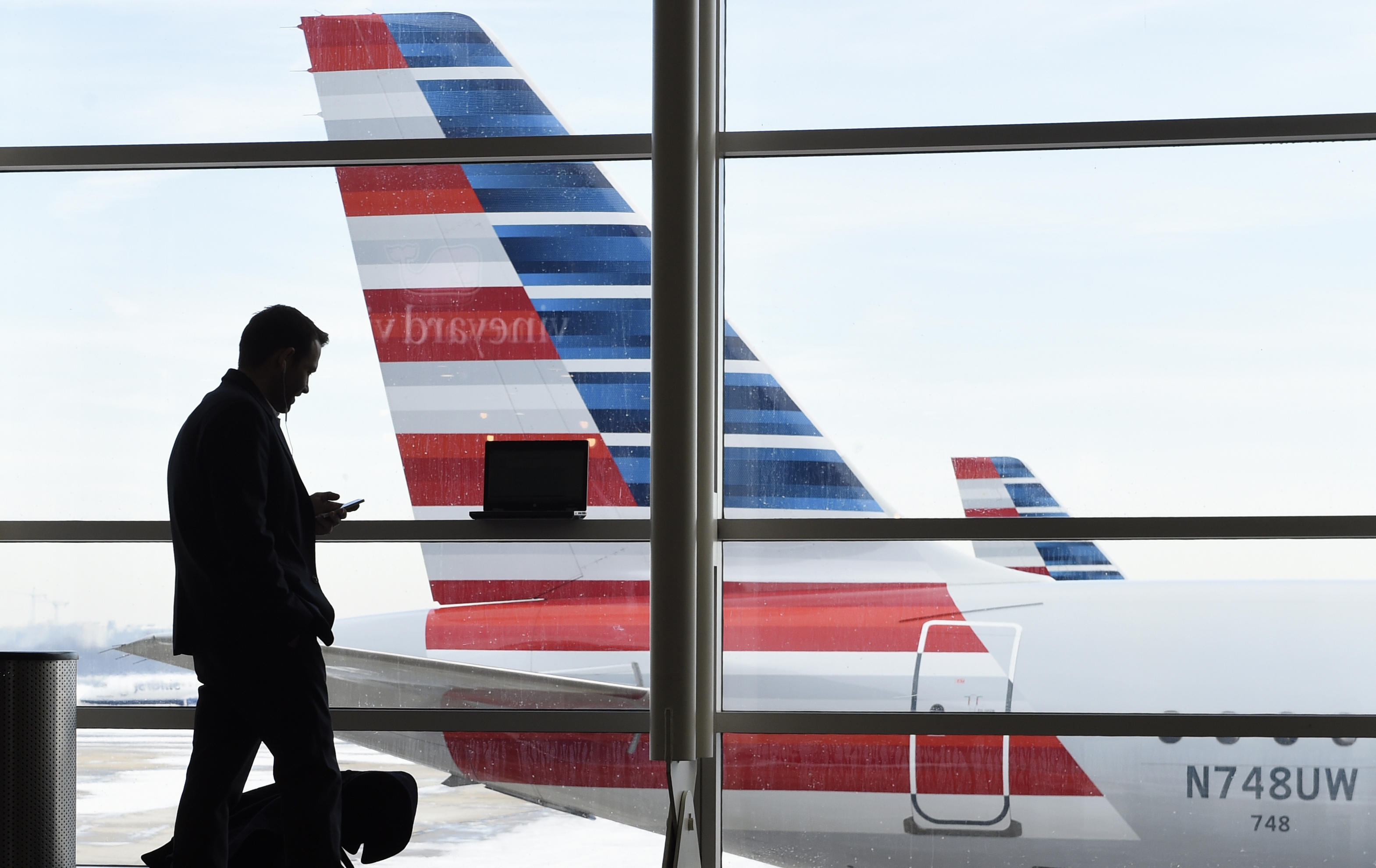 FILE - In this Jan. 25, 2016, file photo, a passenger talks on the phone as American Airlines jets sit parked at their gates at Washington's Ronald Reagan National Airport. American Airlines announced Wednesday, Jan. 18, 2017, that passengers will be able to buy “basic economy” tickets starting in February that will be similar to bare-bones fares already offered by Delta Air Lines and soon to be matched by United Airlines. The basic-economy fares will have a lower price, but will offer fewer comforts. (AP Photo/Susan Walsh, File) (AP)