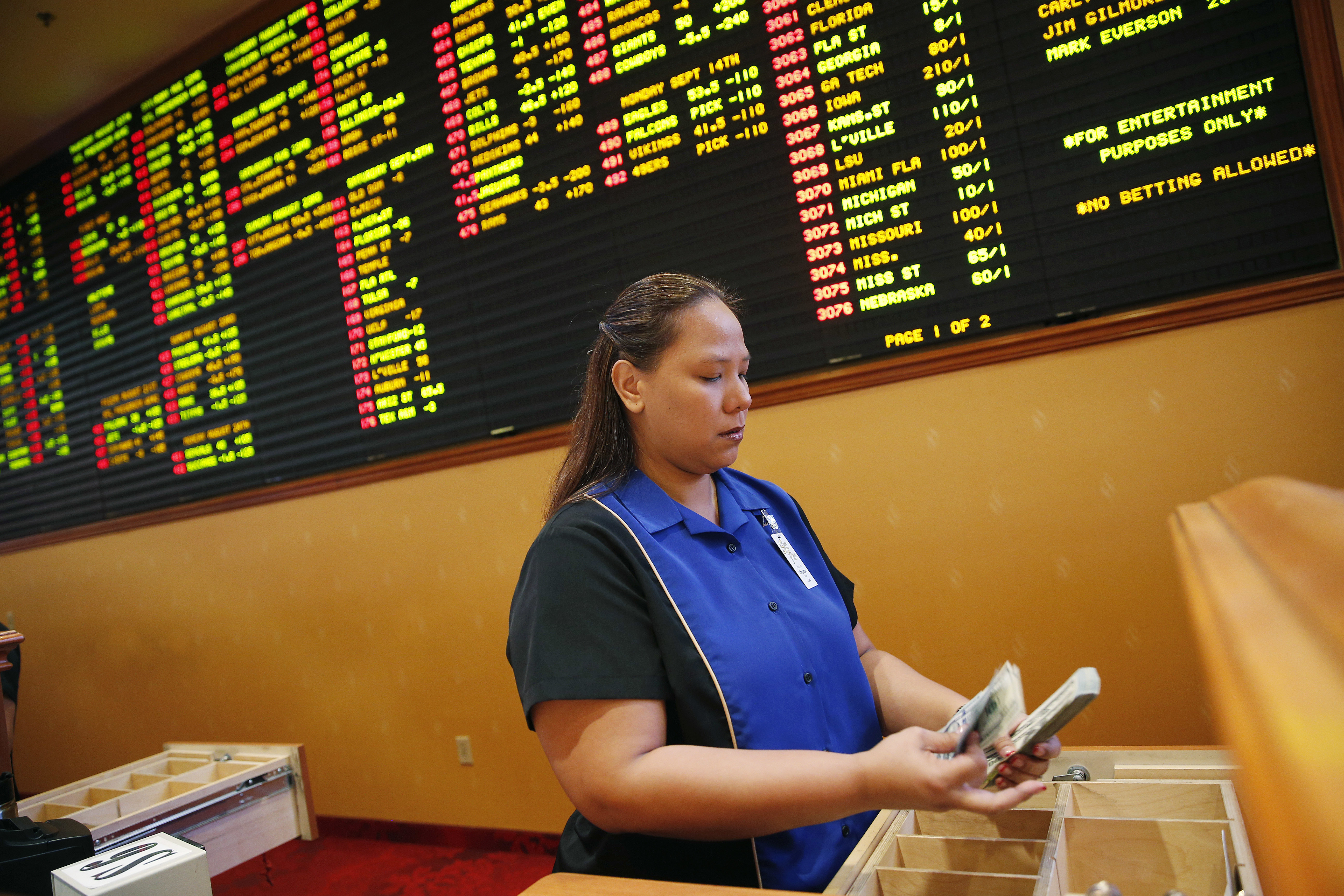 FILE - In this Aug. 20, 2015, file photo, Therese Duenas counts money as she takes bets in the sports book at the South Point hotel and casino in Las Vegas. On the board behind here are odds on NFL football and other bets. Once upon a time, the thought of gambling on a pro football game brought gasps of indignation from the NFL offices. And swift action if it was a player who actually placed a bet. The Oakland Raiders’ new stadium could literally be walking distance from a few of the city’s dozens of sports books. (AP Photo/John Locher, File) (AP)