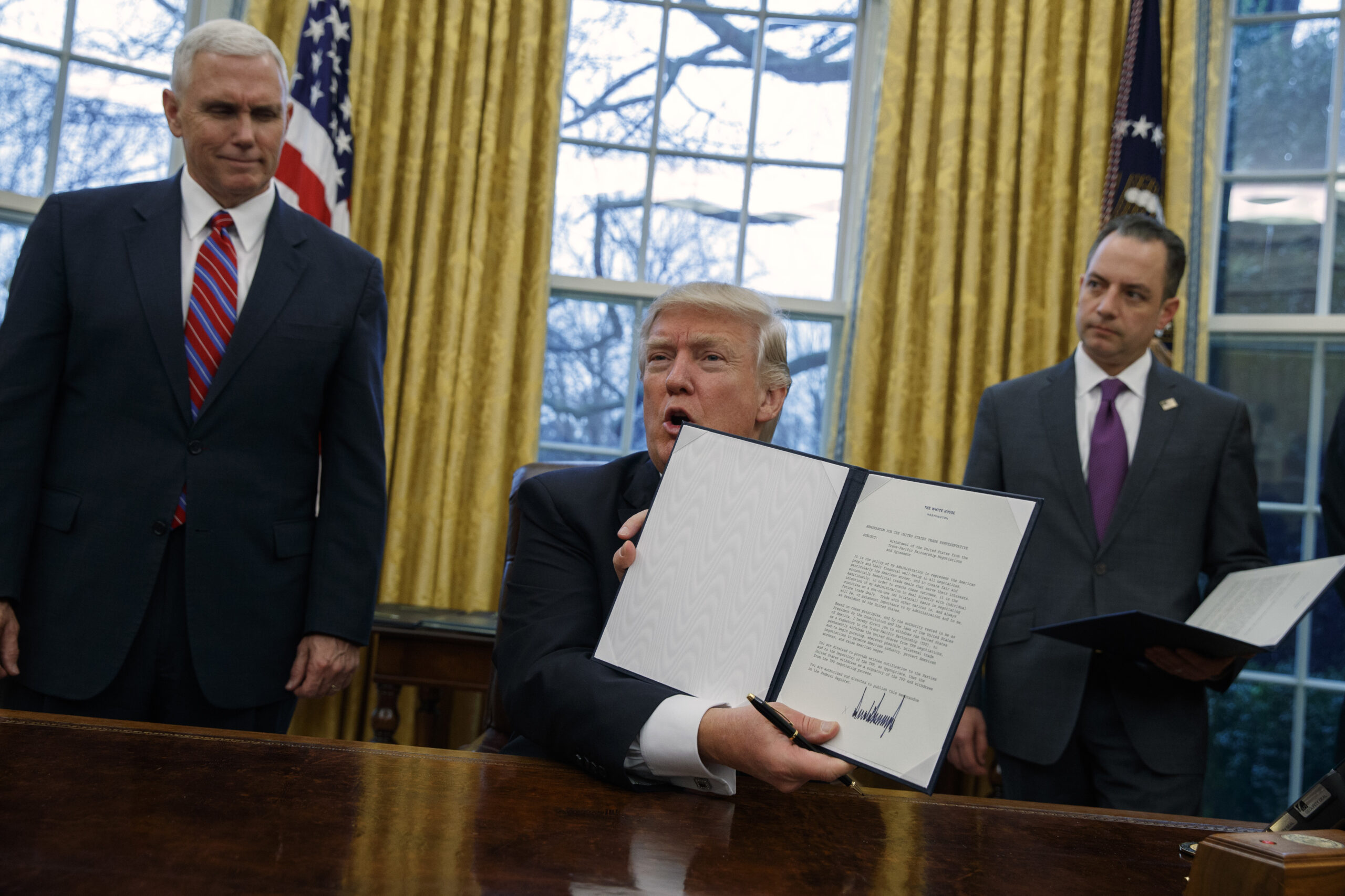 Vice President Mike Pence, left, and White House Chief of Staff Reince Priebus watch as President Donald Trump shows off an executive order to withdraw the U.S. from the 12-nation Trans-Pacific Partnership trade pact agreed to under the Obama administration, Monday, Jan. 23, 2017, in the Oval Office of the White House in Washington. (AP Photo/Evan Vucci) (AP)