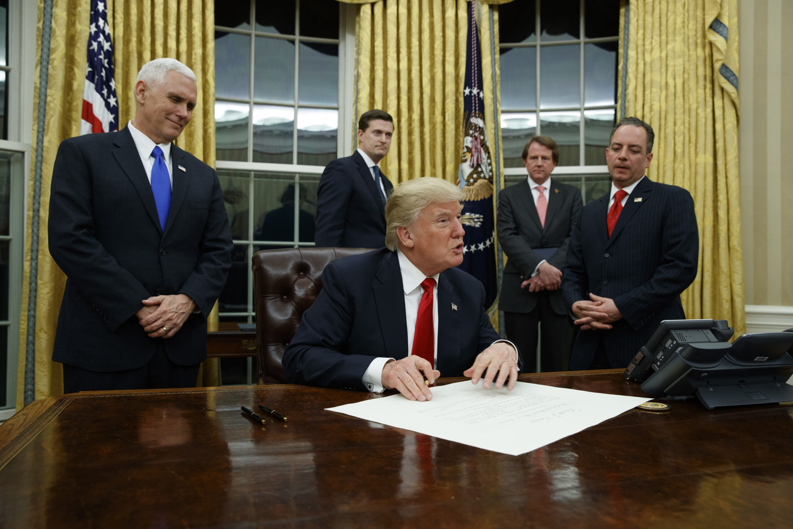 Vice President Mike Pence watches at left as President Donald Trump prepares to sign his first executive order, Friday, Jan. 20, 2017, in the Oval Office of the White House in Washington. (AP Photo/Evan Vucci) (AP)