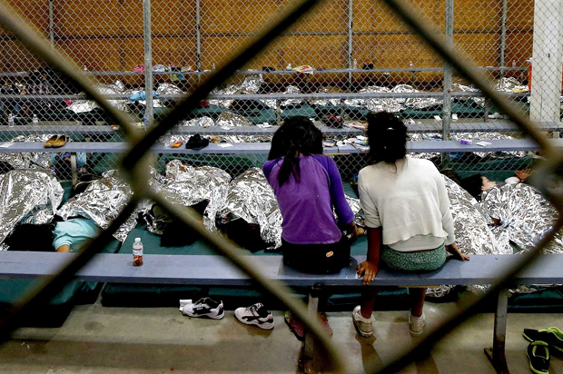 Two young girls watch television from their holding area where hundreds of mostly Central American immigrant children are being processed and held at the U.S. Customs and Border Protection Nogales Placement Center (AP/Ross D. Franklin)