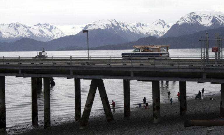 In this May 24, 2015, photo a vehicle drives on a pier to be loaded onto an Alaska state ferry while people fish underneath the pier in Homer, Alaska. (AP Photo/Mark Thiessen)
