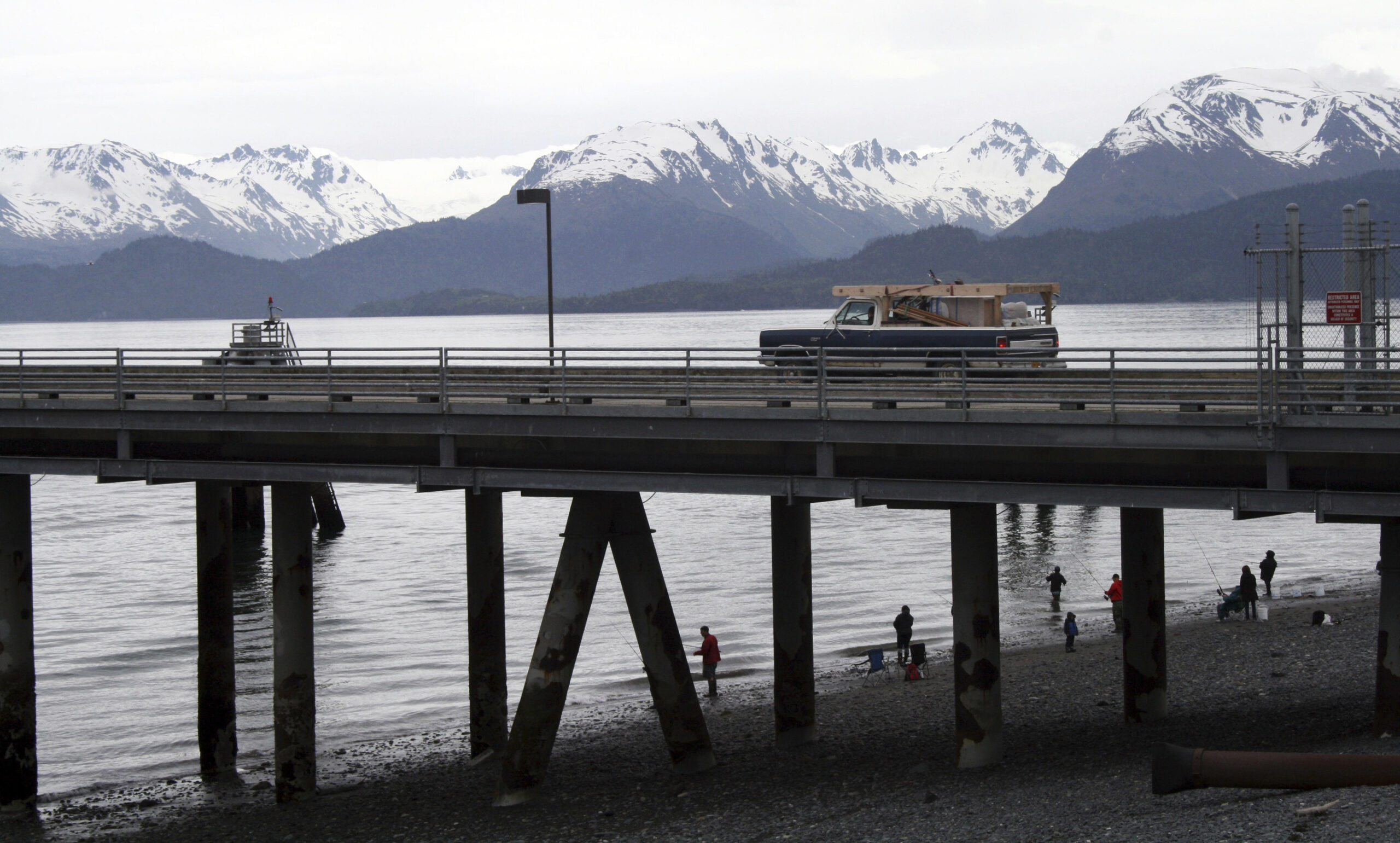 In this May 24, 2015, photo a vehicle drives on a pier to be loaded onto an Alaska state ferry while people fish underneath the pier in Homer, Alaska. (AP Photo/Mark Thiessen)