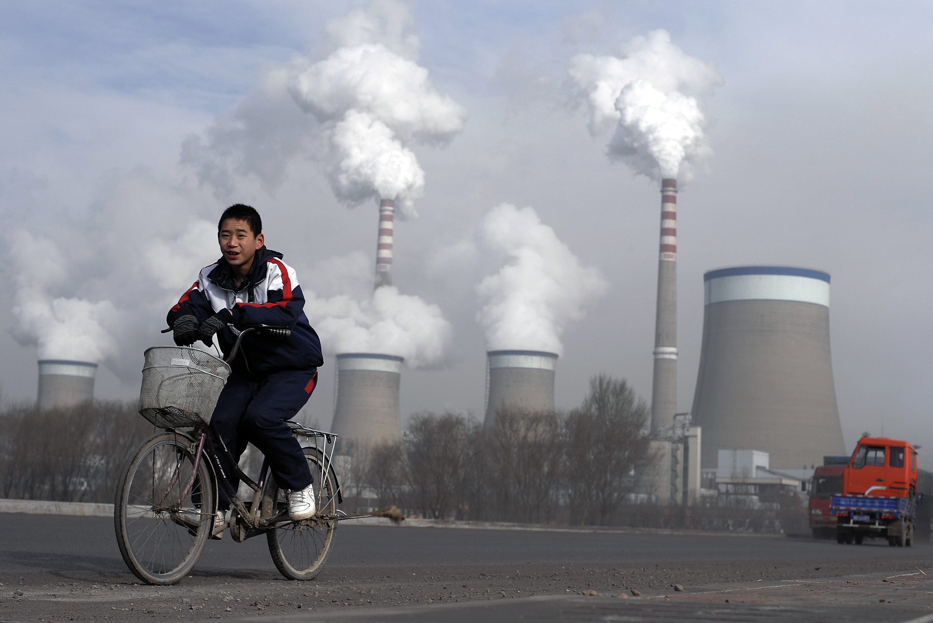 FILE - In this Dec. 3, 2009 file photo, a Chinese boy cycles past cooling towers of a coal-fired power plant in Dadong, Shanxi province, China. Led by cutbacks in China and India, construction of new coal-fired power plants is falling worldwide, improving chances climate goals can be met despite earlier pessimism, three environmental groups said Wednesday, March 22, 2017. (AP Photo/Andy Wong, File) (AP)
